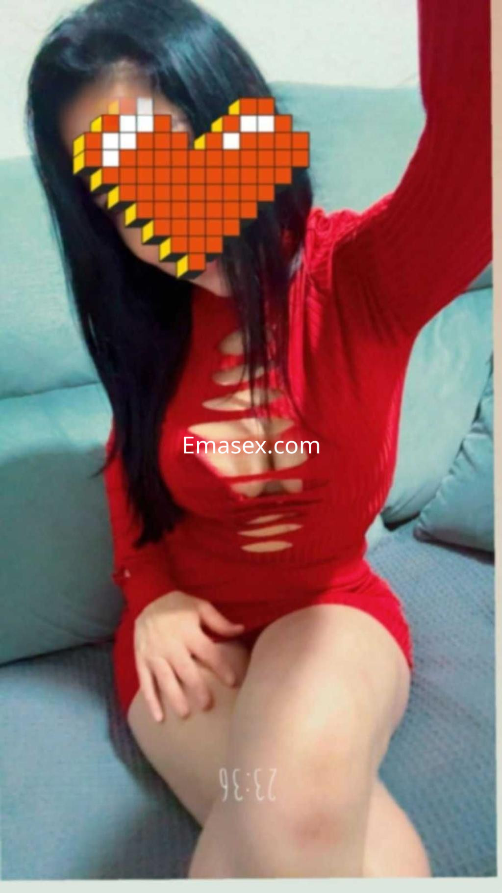 Escort en Badajoz con vestido rojo ajustado y cabello largo, posando sentada en un sofá.