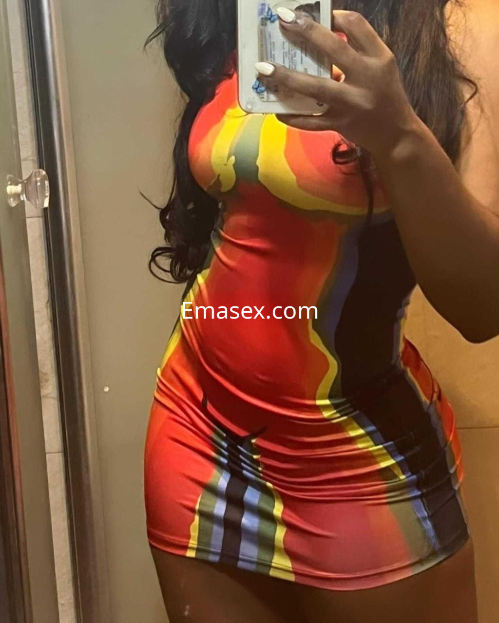 La puta en Badajoz se muestra con un vestido ajustado y colorido, destacando su figura en un espejo.