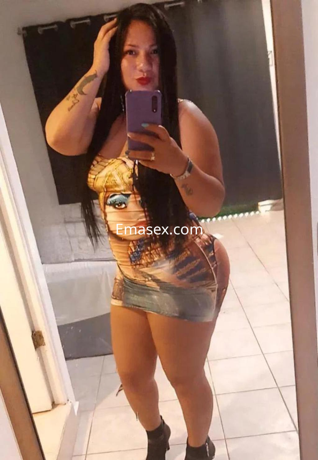 Puta en Burgos con vestido ajustado de estampado llamativo, posando frente al espejo en un ambiente interior.