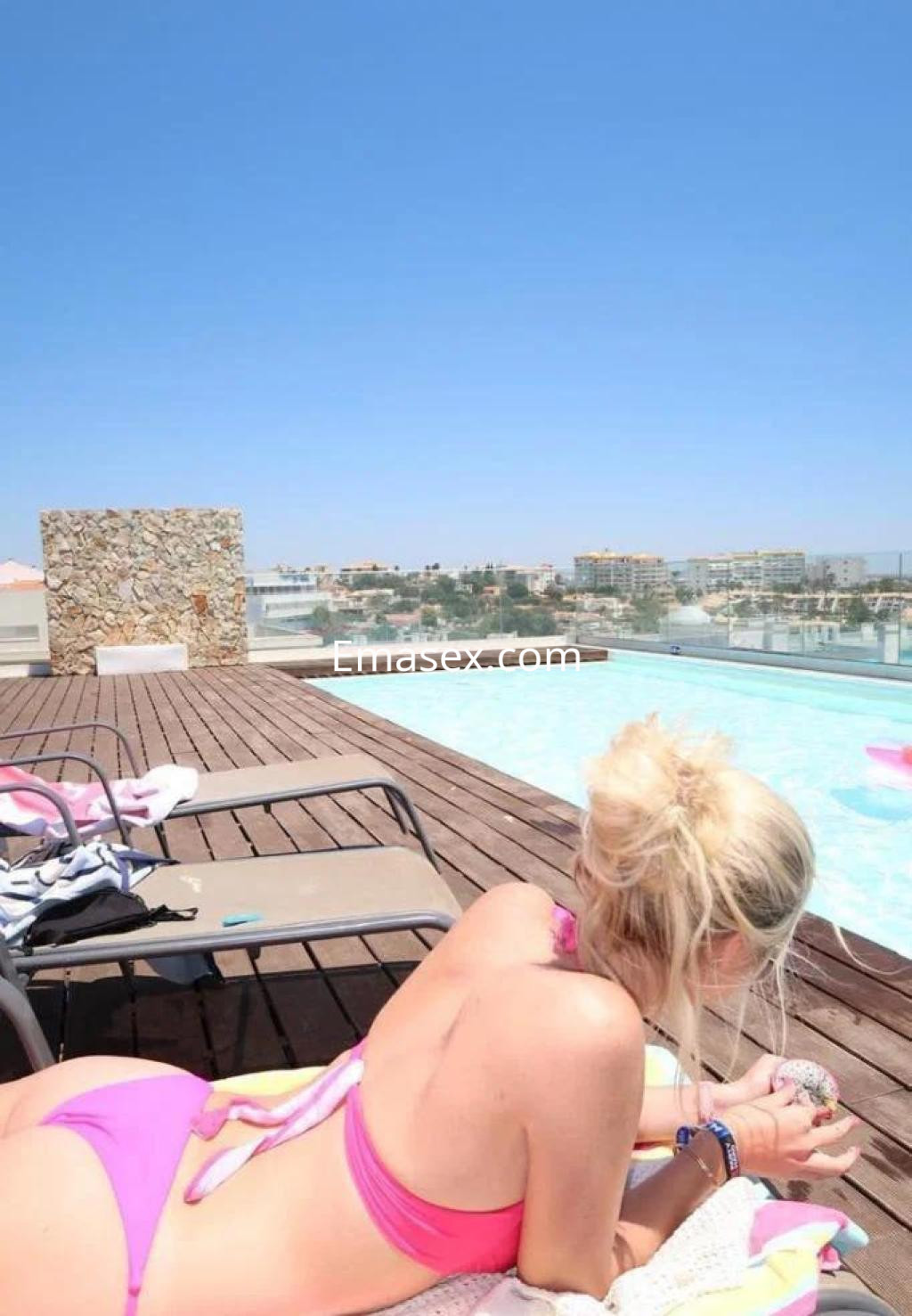 Escort en Cáceres, relajándose junto a una piscina, con un bikini rosa y el cabello recogido.