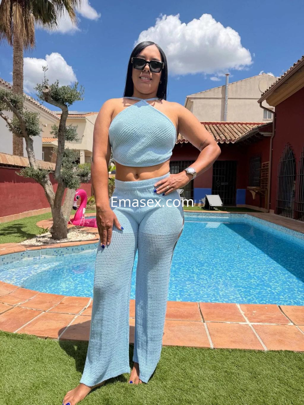 Escort en Granada con un conjunto azul claro, posando junto a una piscina en un entorno al aire libre.