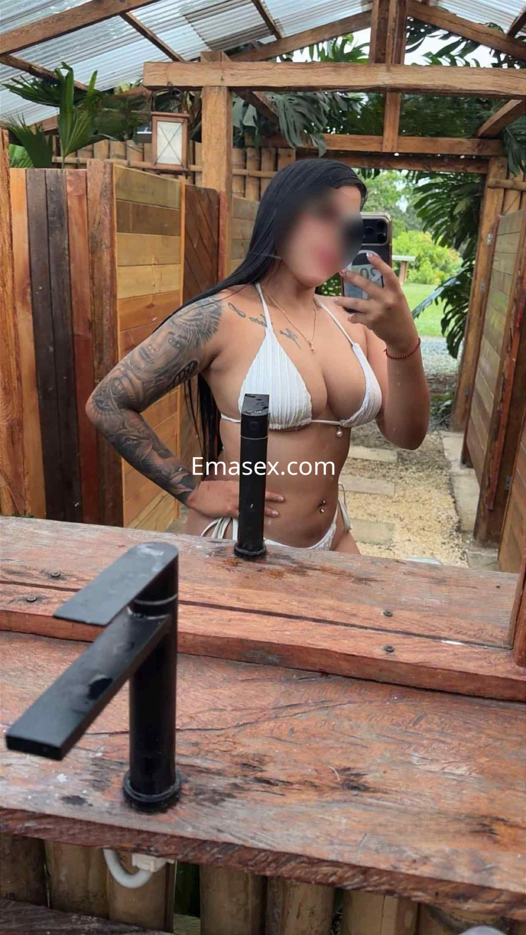 Escort en Granada posando frente a un espejo, vistiendo un bikini blanco y mostrando un tatuaje en el brazo.