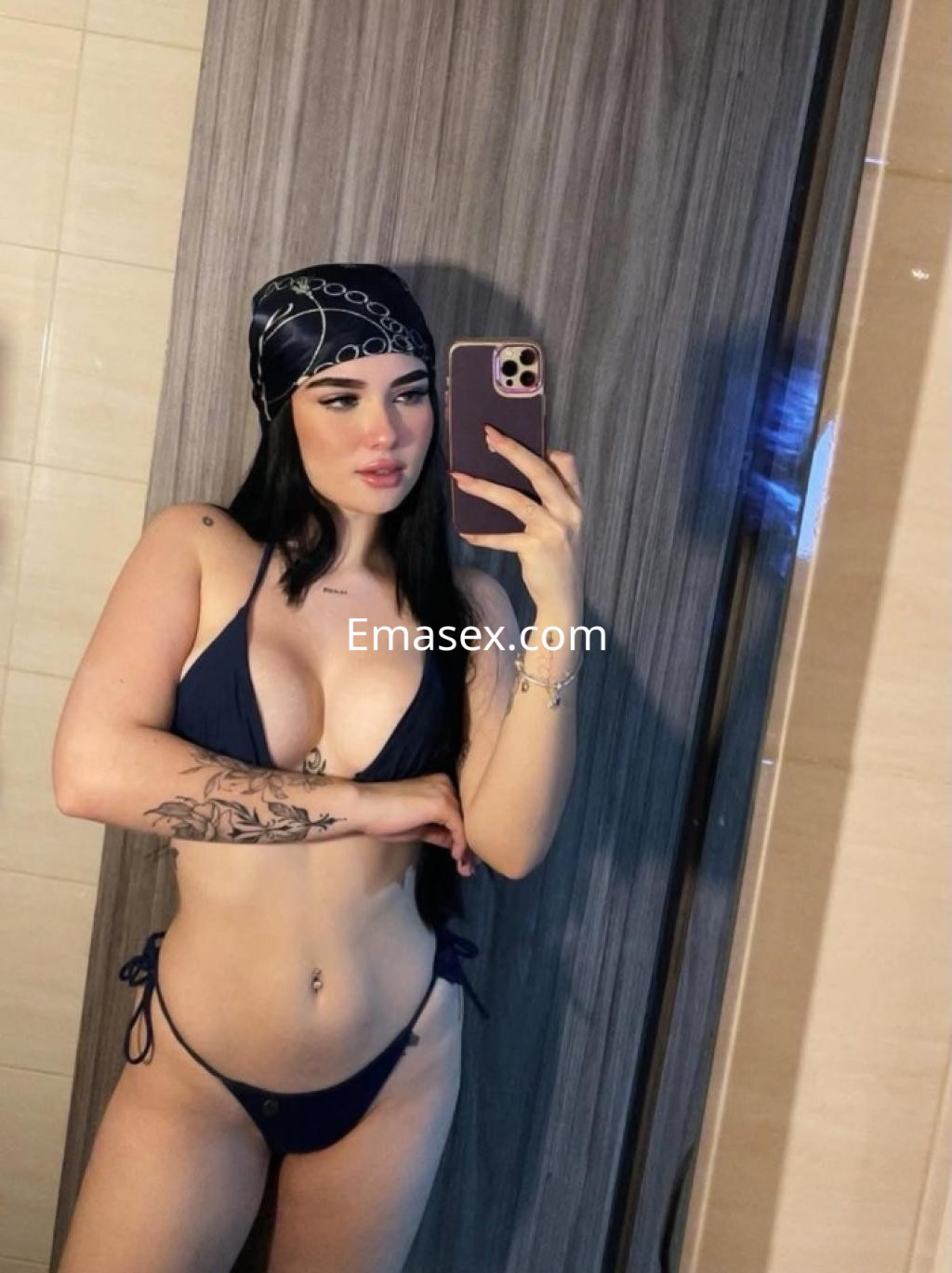 Escort en Granada luciendo un bikini oscuro y un pañuelo en la cabeza, posando frente al espejo.