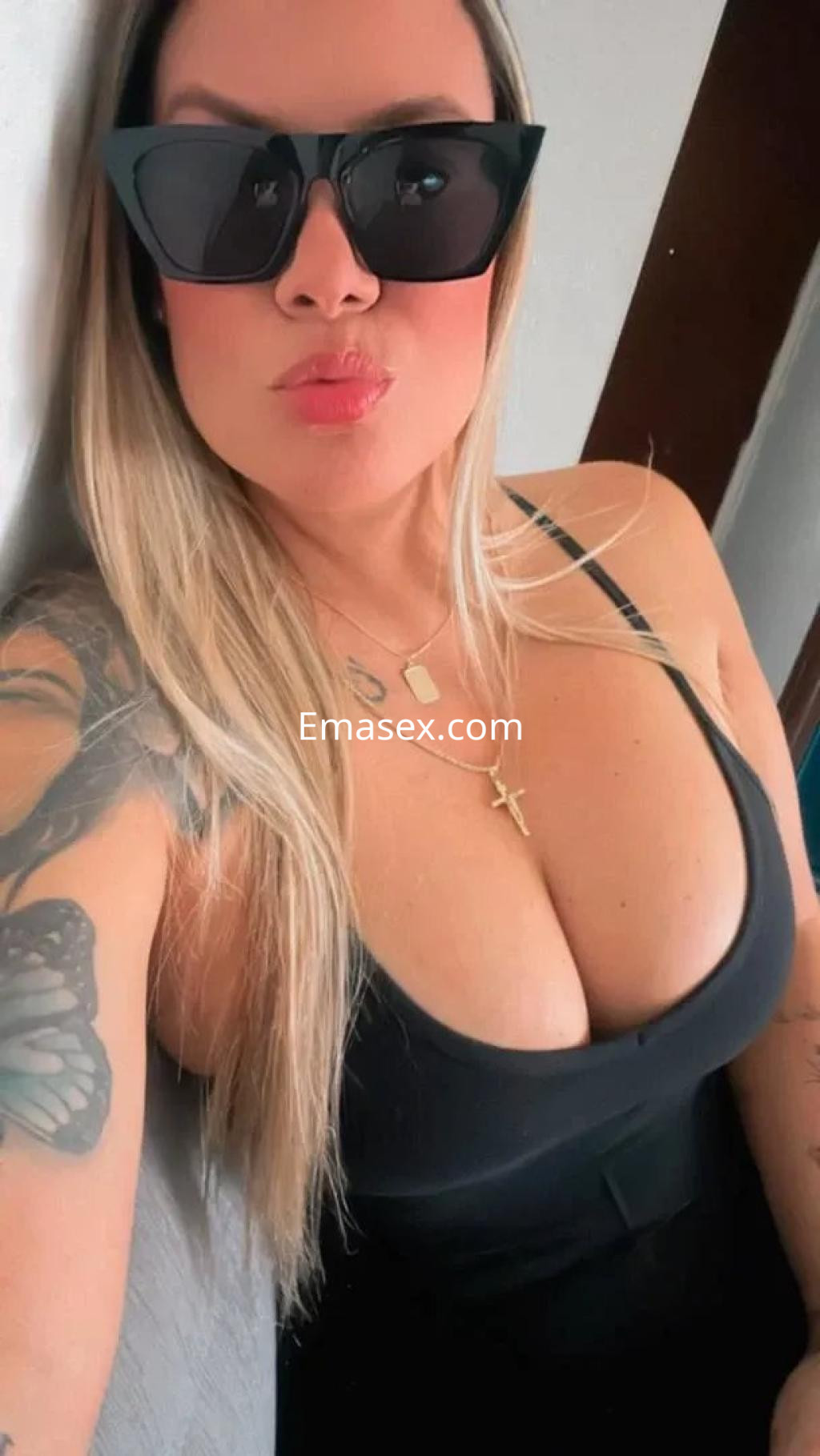 Escort en Murcia con cabello rubio y largo, luciendo gafas de sol negras y un vestido ajustado, posando con confianza.