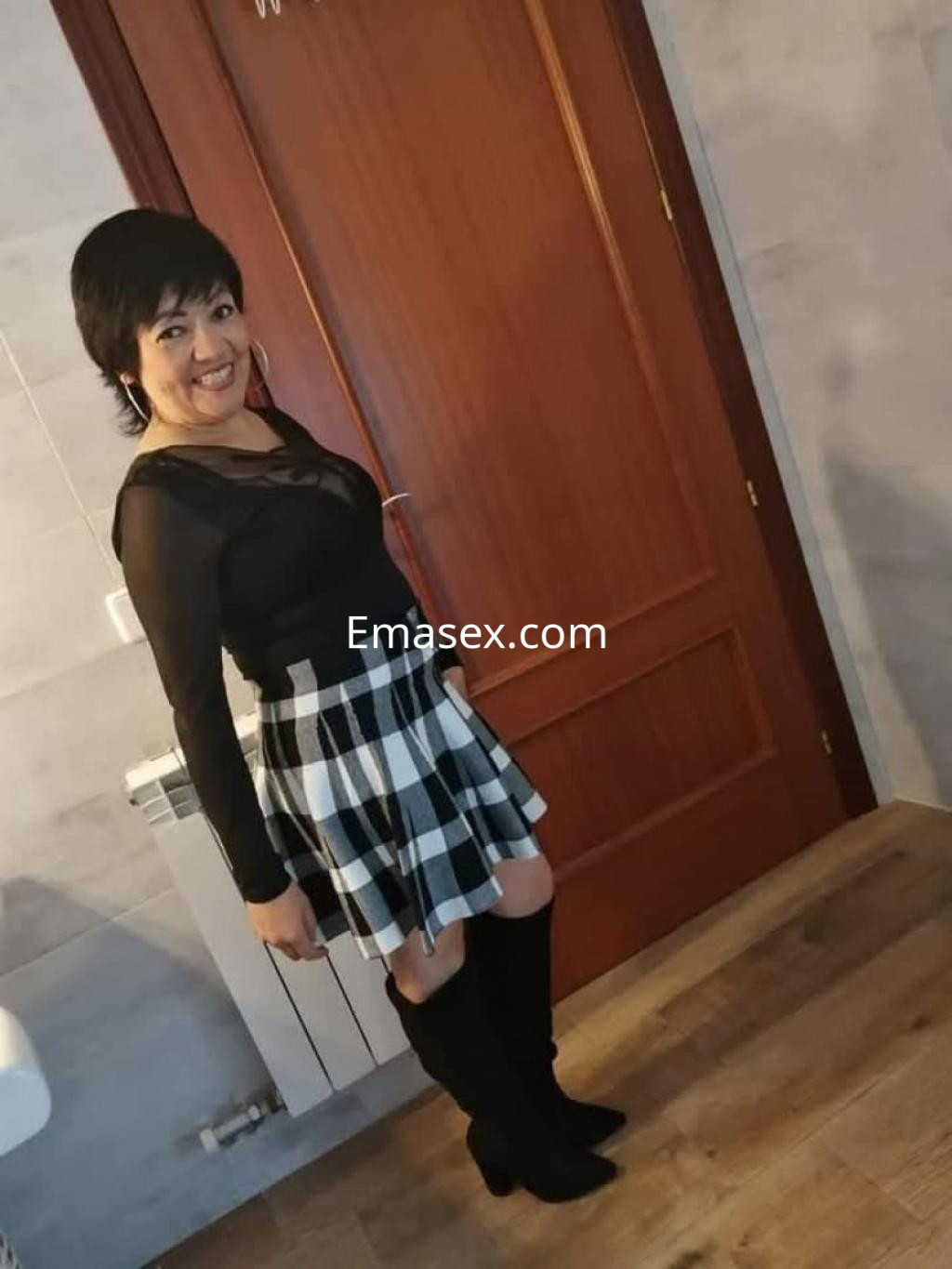 La puta aparece en un vestido negro con mangas transparentes y una falda de cuadros, posando en un ambiente interior de Murcia.