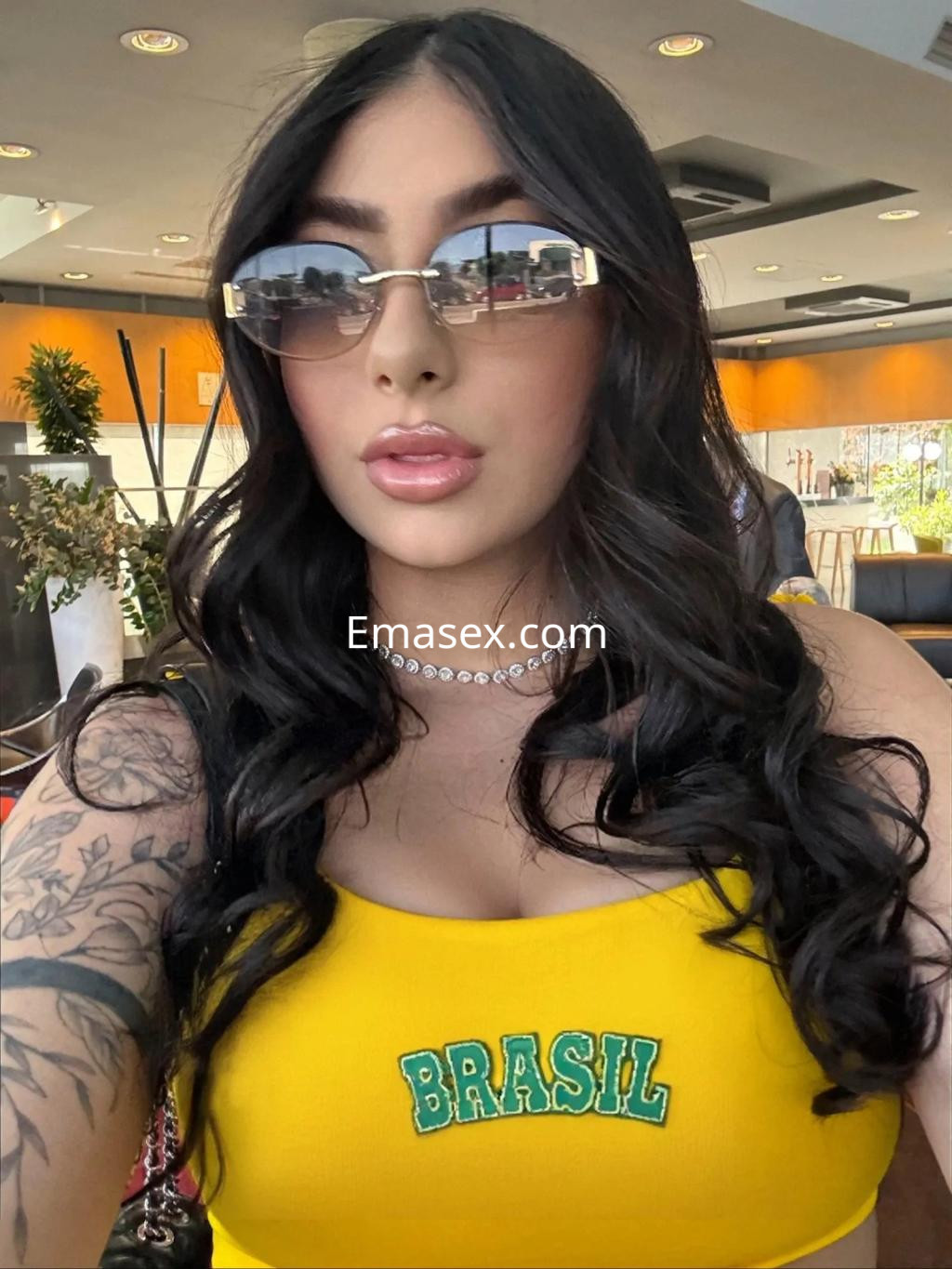 La escort en Oviedo se retrata en un ambiente moderno, vistiendo una blusa amarilla con la palabra 