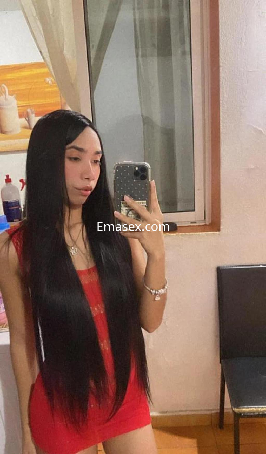 Escort en Sevilla con cabello largo y lacio, vistiendo un vestido rojo, posando frente a un espejo.