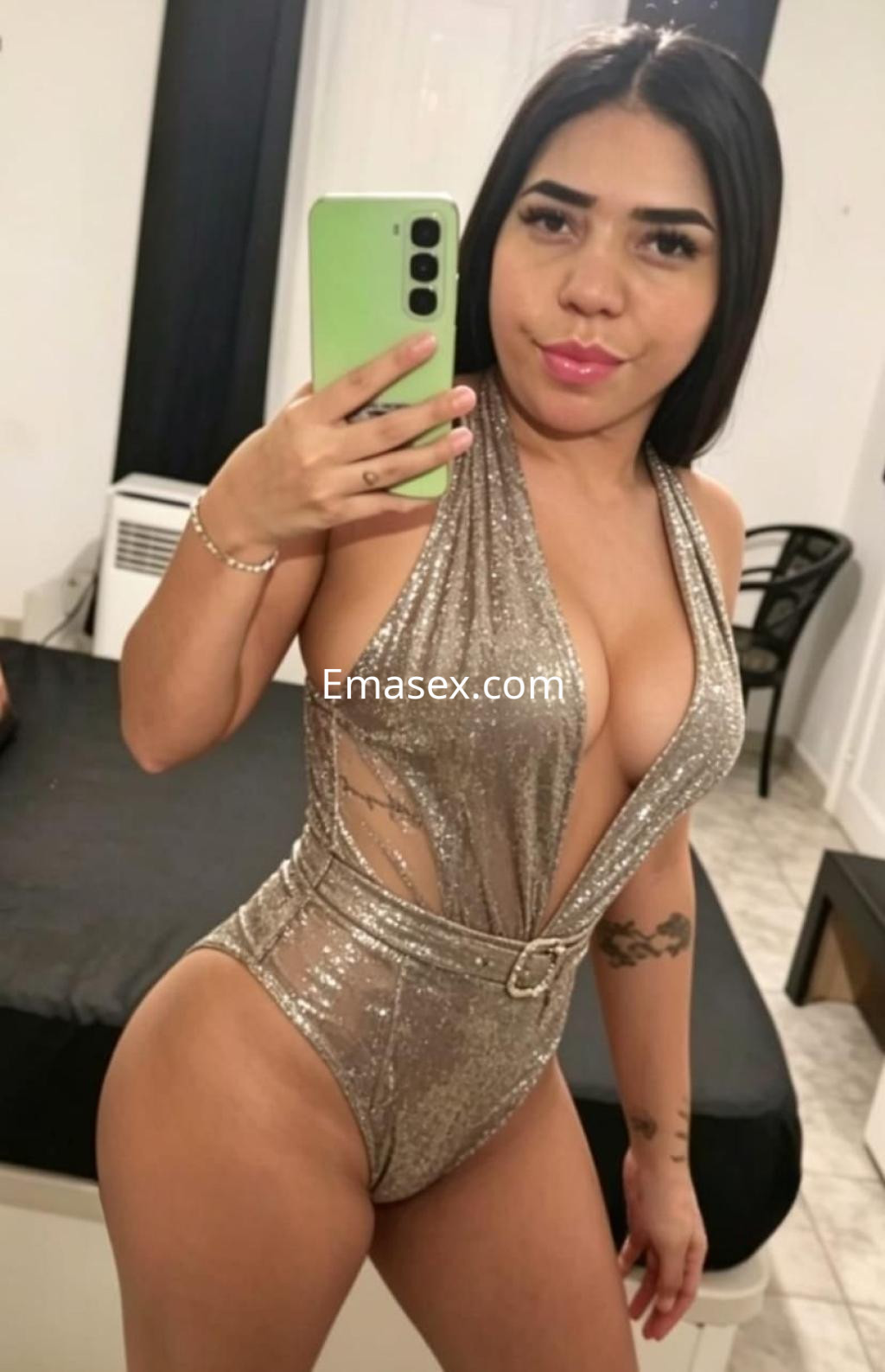 La escort en Tarragona se muestra en un body brillante y ajustado, posando con un teléfono en la mano.
