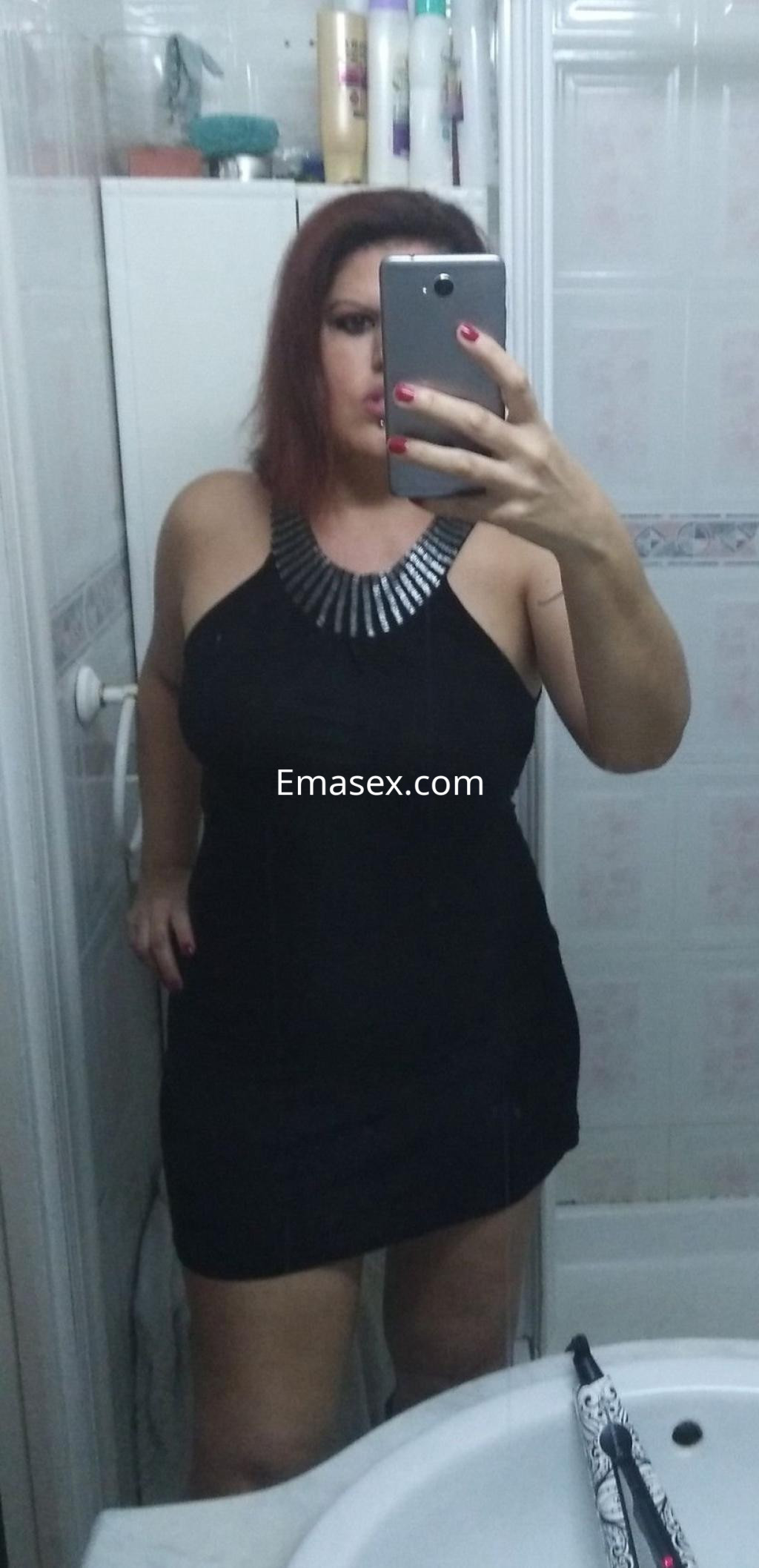 Escort en Málaga con un vestido negro ajustado y collar plateado, posando frente al espejo en un baño.