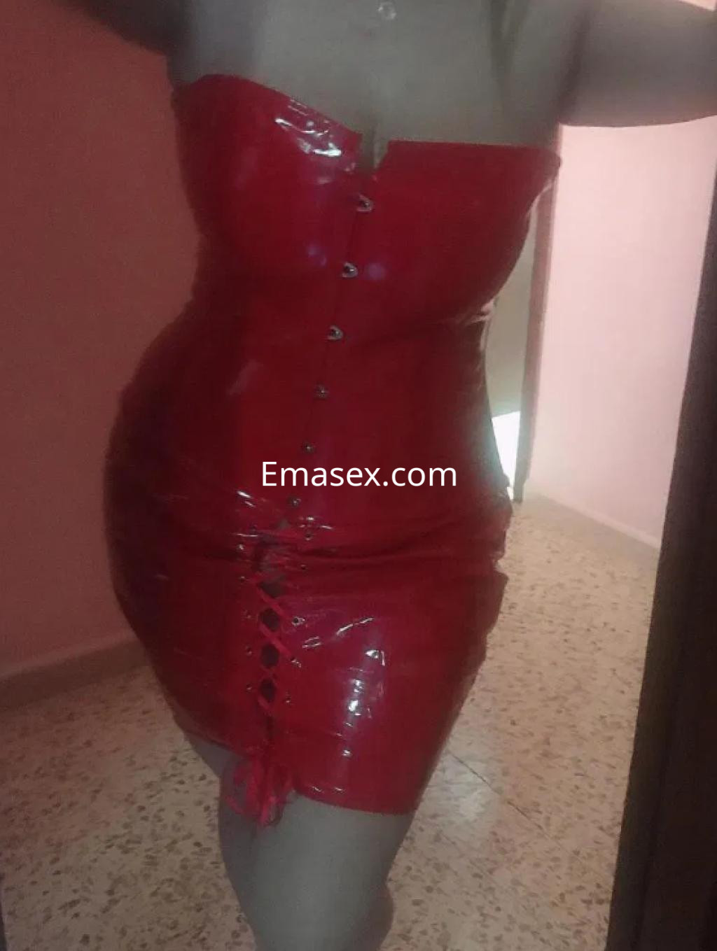 Puta en Tarragona viste un ajustado vestido rojo de látex que resalta su figura en un entorno interior.