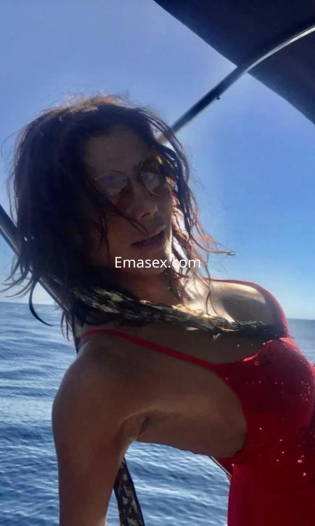Escort posando en un barco con un bañador rojo, cabello suelto y fondo de mar en Málaga.