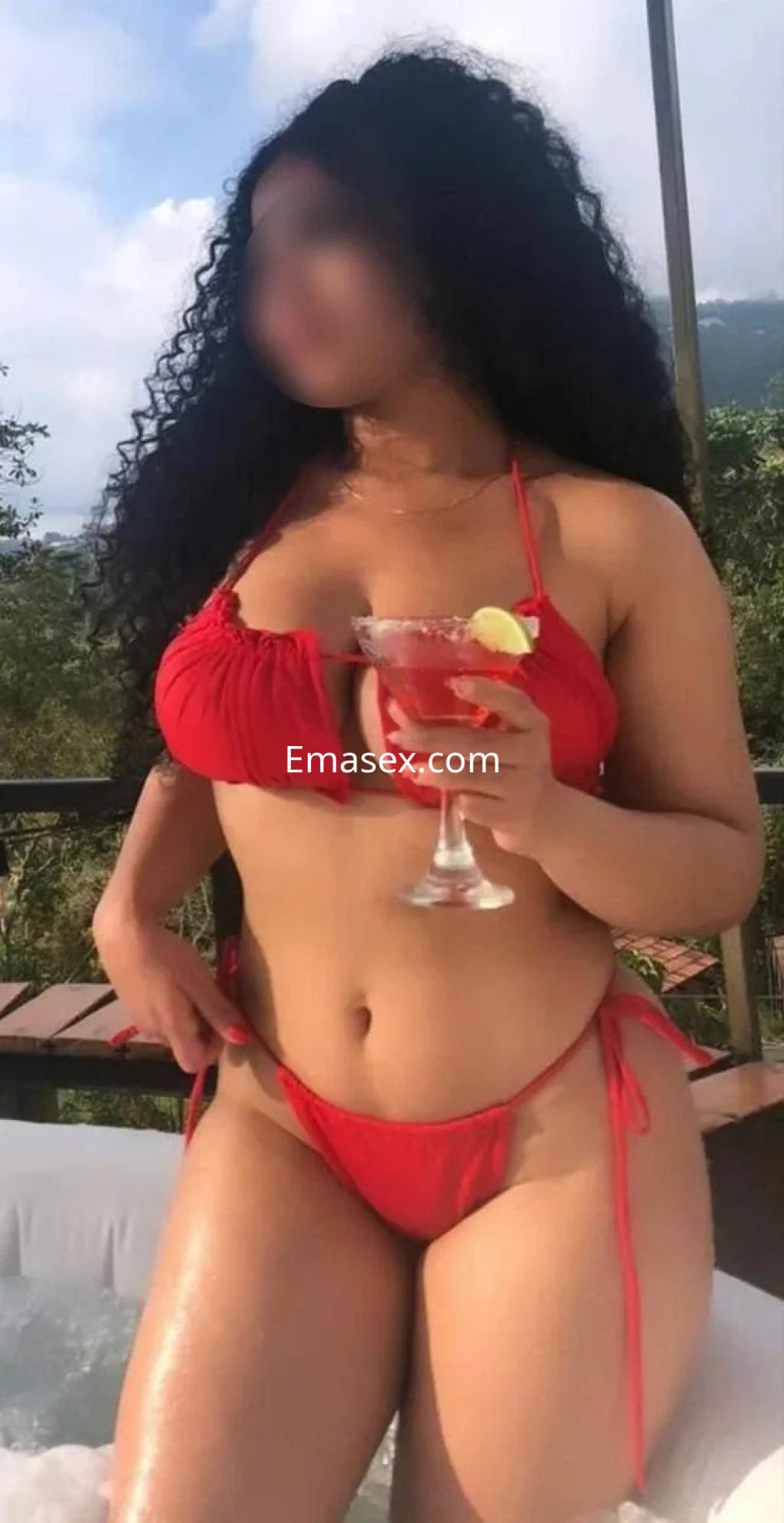 La puta en Málaga lleva un bikini rojo y sostiene un cóctel mientras posando junto a una piscina.