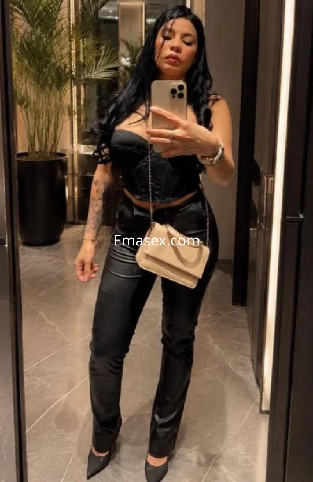 Escort posando en un espejo con un top negro y pantalones ajustados en un elegante entorno de Girona.