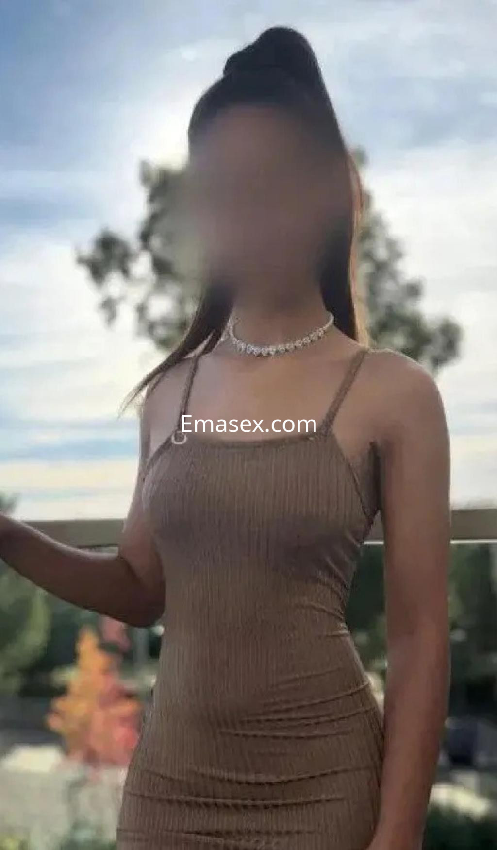 Escort en Vigo viste un vestido ajustado de color marrón claro, con un peinado recogido y collar elegante.