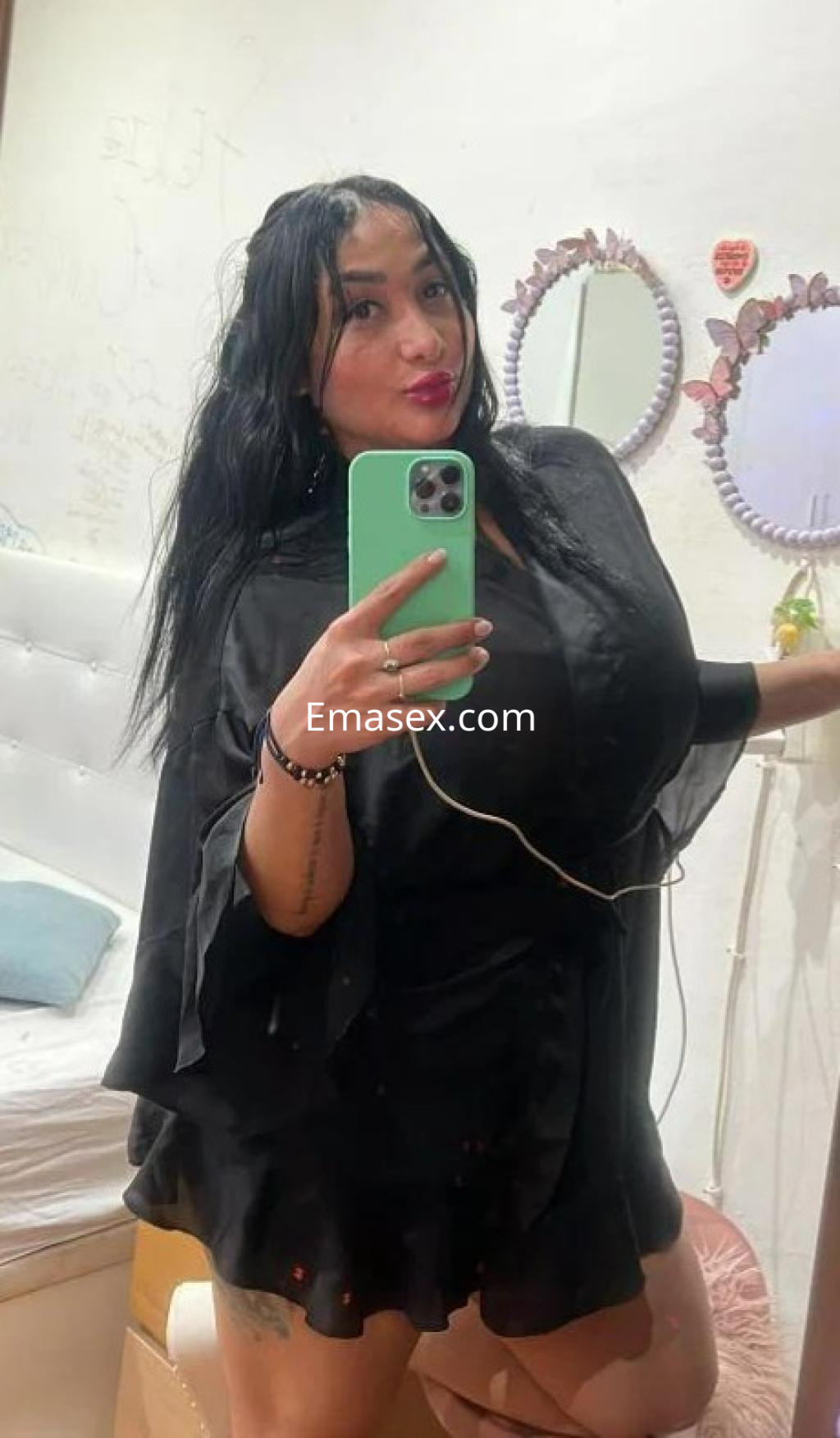 Escort en Barcelona posando frente a un espejo, viste una prenda negra y lleva el cabello largo y suelto.