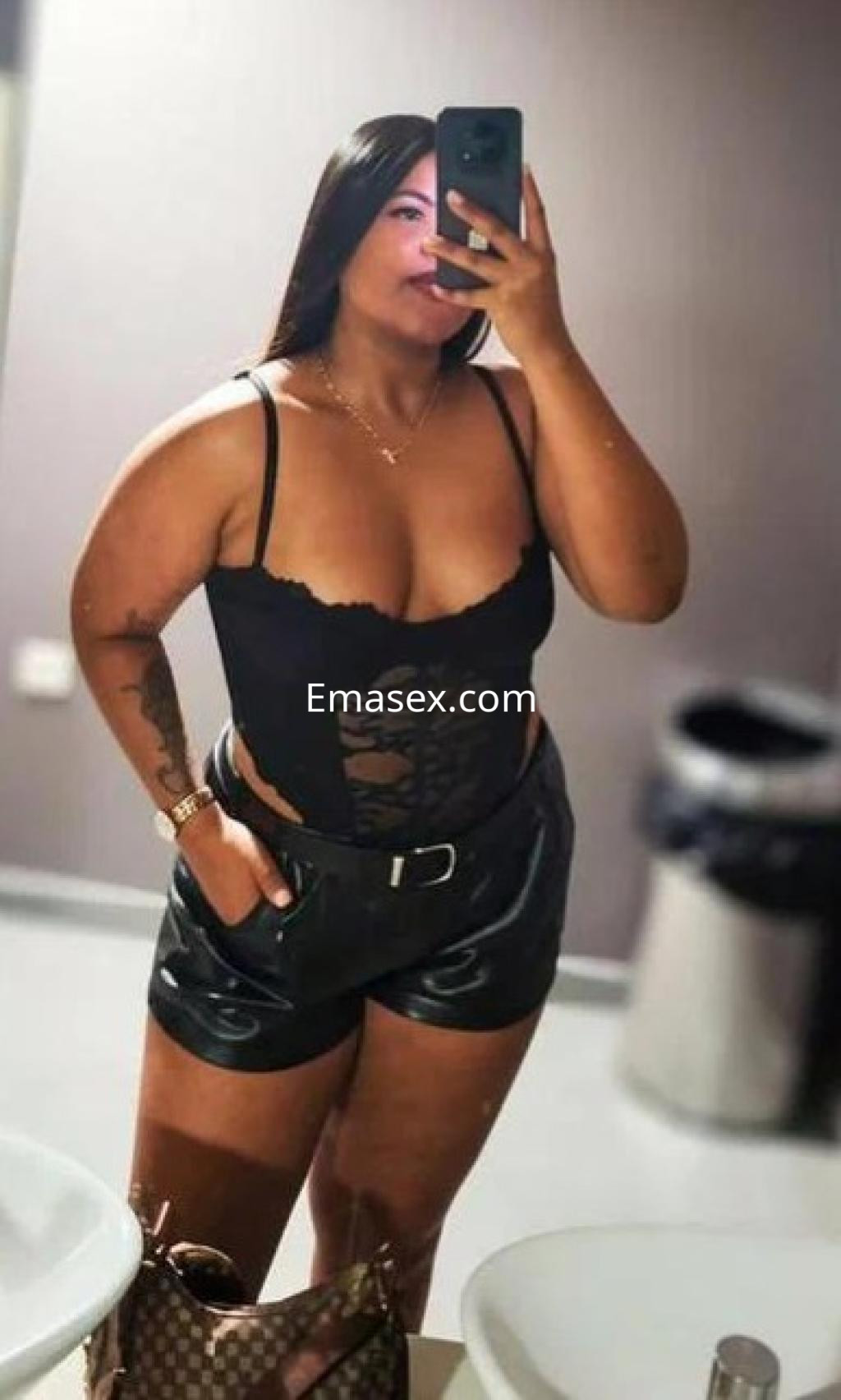 Puta en Coruña, posando frente al espejo con un body negro y pantalones cortos de cuero, mostrando su figura.