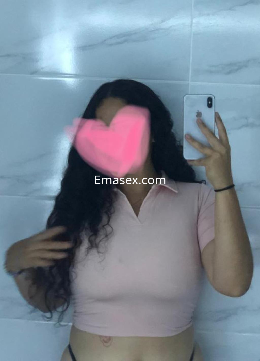 Escort en Oviedo con cabello rizado y largo, vistiendo una blusa rosa y mostrando una pose en un baño.