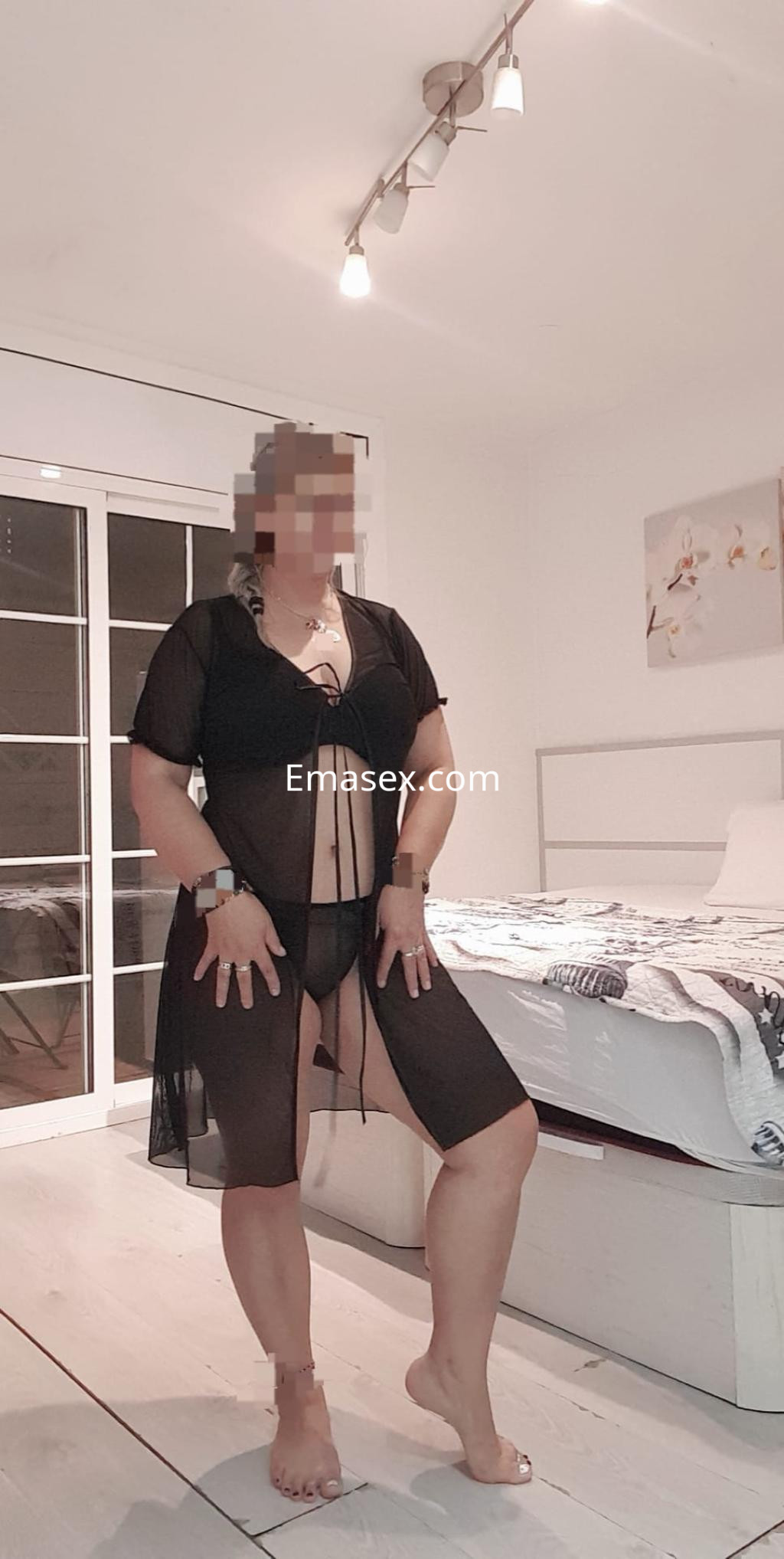 La puta viste una lencería negra transparente y posa en una habitación luminosa de Barcelona.