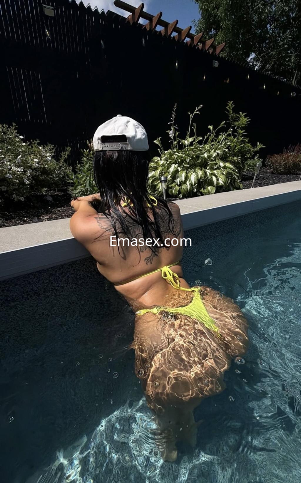 Puta con cabello oscuro y lacio, luciendo un bikini amarillo, recostada en la piscina en Sevilla.