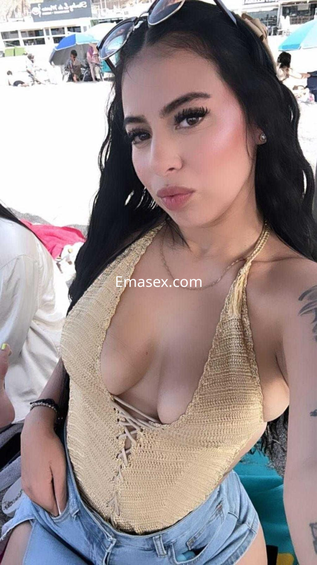 La puta posa en la playa con un traje de baño dorado y pantalones cortos, mostrando su cabello ondulado.