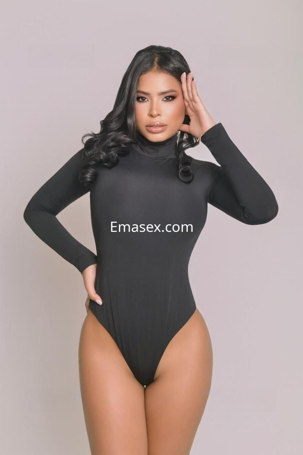 La puta luce un body negro ajustado, con mangas largas y cabello negro ondulado, en un fondo neutro en Ibiza.
