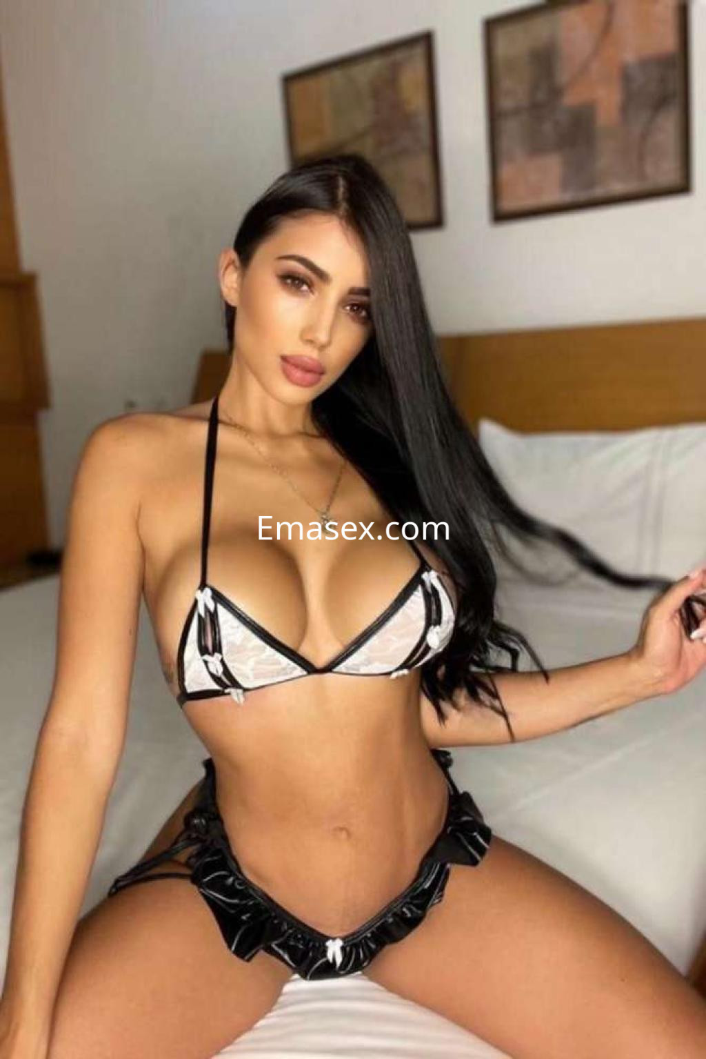 Escort en Ibiza con cabello largo y lacio, vistiendo un bikini blanco y negro, posando en una habitación.