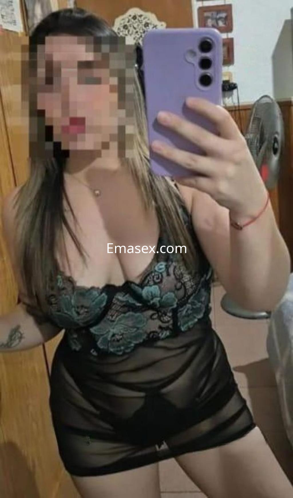 La puta posa en un ambiente interior con un vestido negro semitransparente y detalles en verde, en Ibiza.