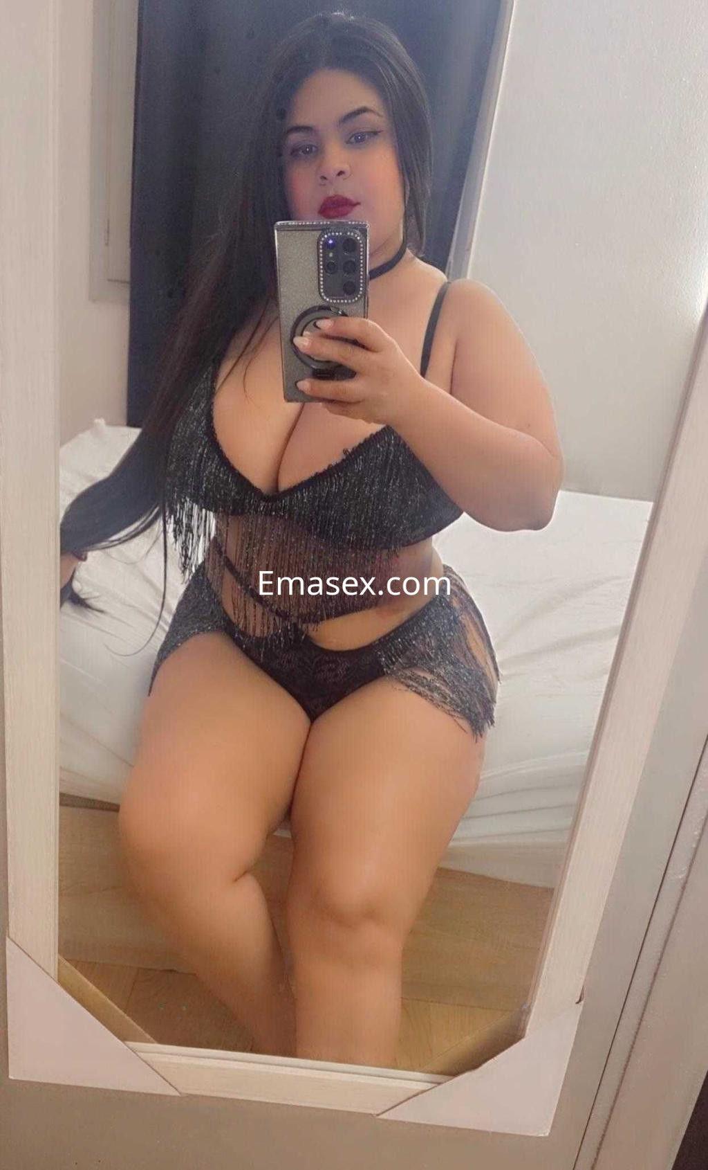 Puta posando frente al espejo en Ibiza, con un conjunto de lencería negra con flecos y cabello largo.