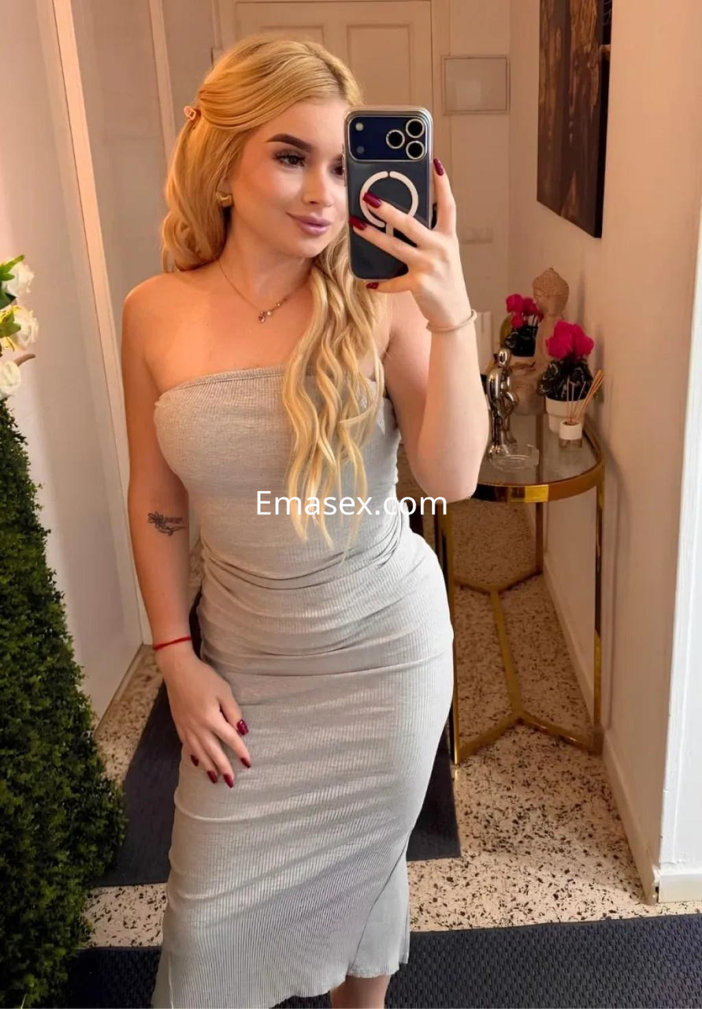 Puta en Palma de Mallorca, posando en un vestido ajustado gris y con cabello largo y rubio, sosteniendo un teléfono.