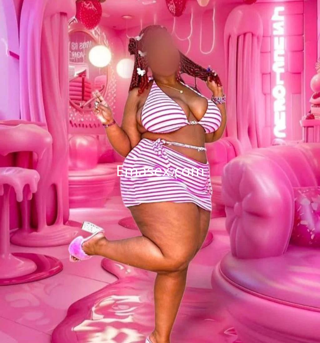 Escort en Barcelona con un conjunto de bikini a rayas en un ambiente rosa y decorado con elementos llamativos.