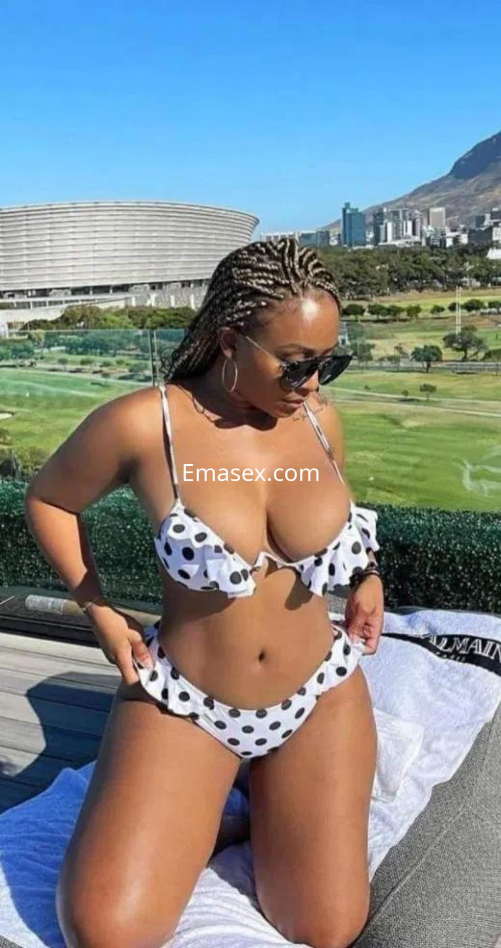 Escort en Girona con cabello trenzado, vistiendo bikini de lunares y gafas de sol, posando en un entorno al aire libre.
