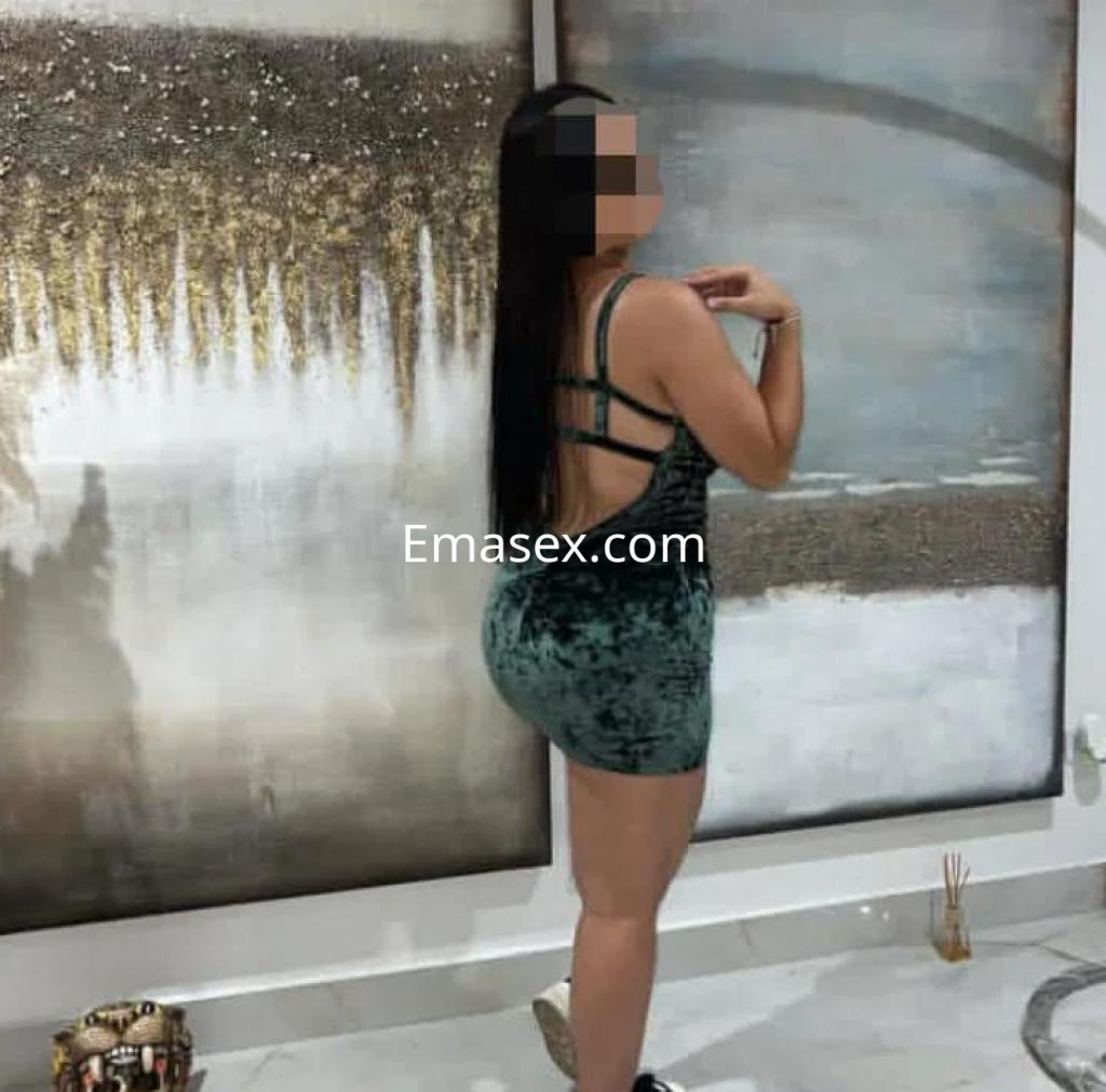 Escort en León posa de espaldas con un vestido de terciopelo verde, mostrando un fondo artístico y decorativo.