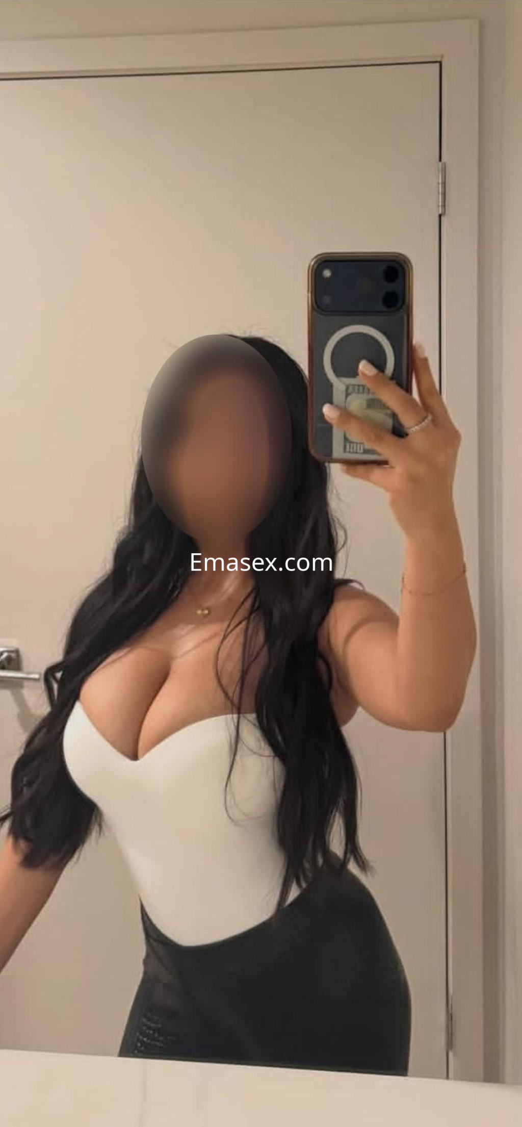 Escort en León con cabello largo y oscuro, viste un body blanco y una falda ajustada negra, posando en un espejo.