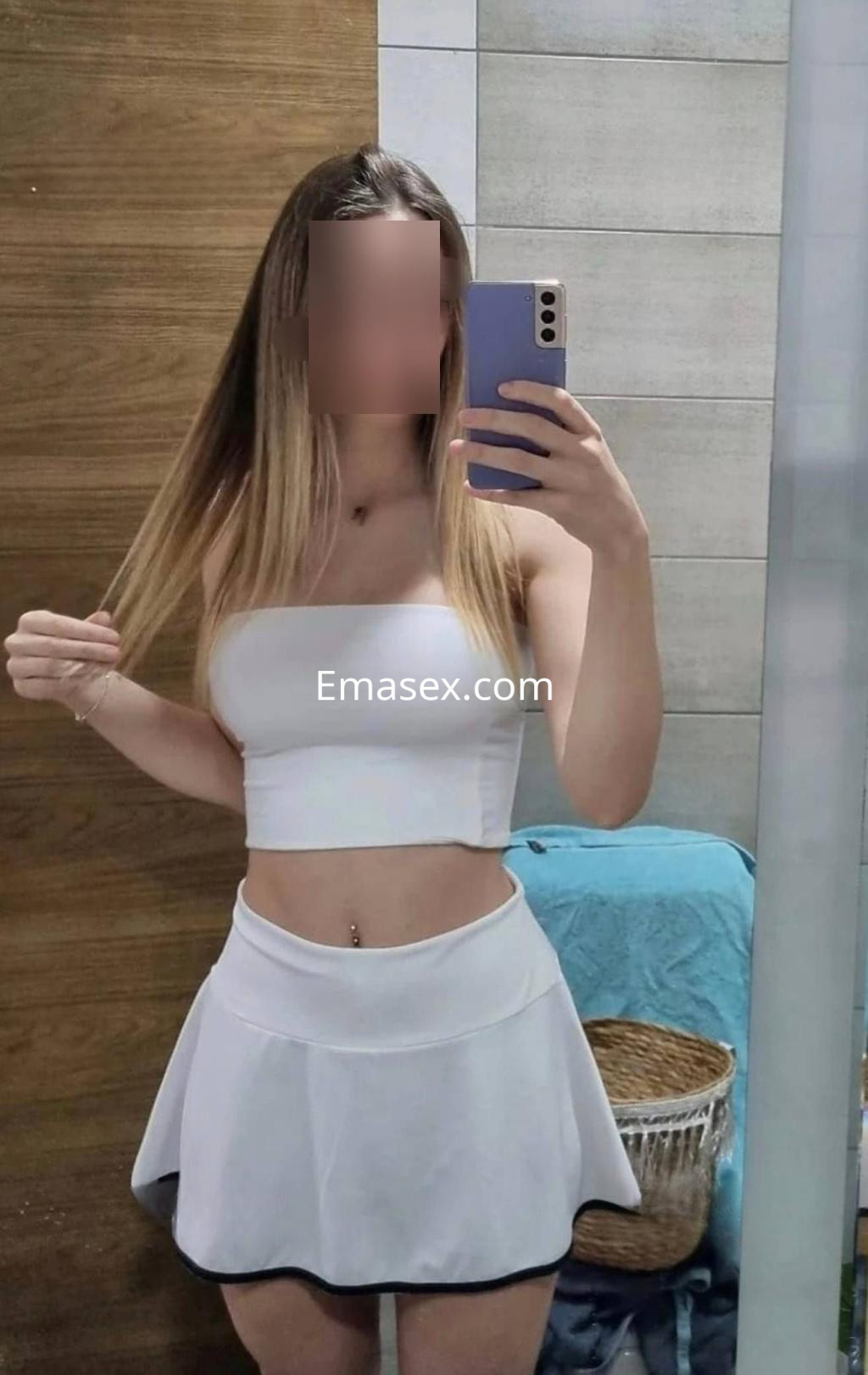 Escort en León con cabello largo y lacio, luciendo un top blanco y una falda corta, posando frente al espejo.
