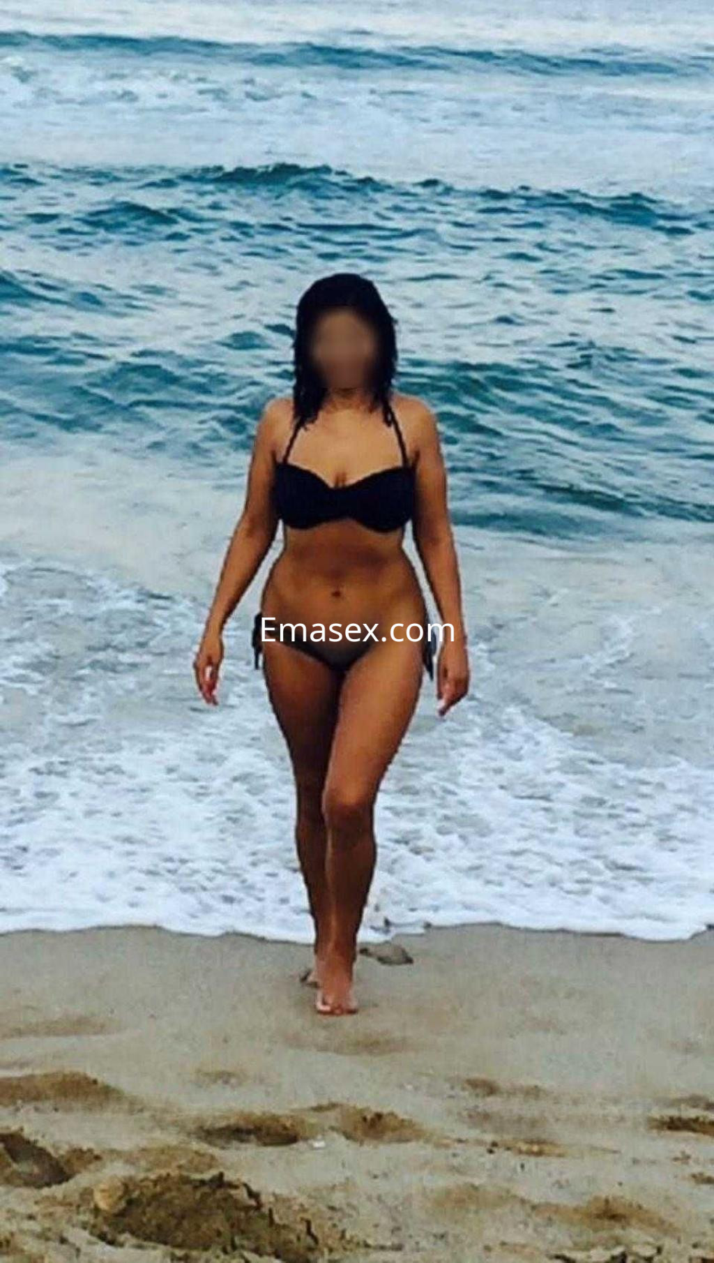 Puta camina hacia la orilla del mar en Murcia, vistiendo un bikini negro y luciendo una piel bronceada.