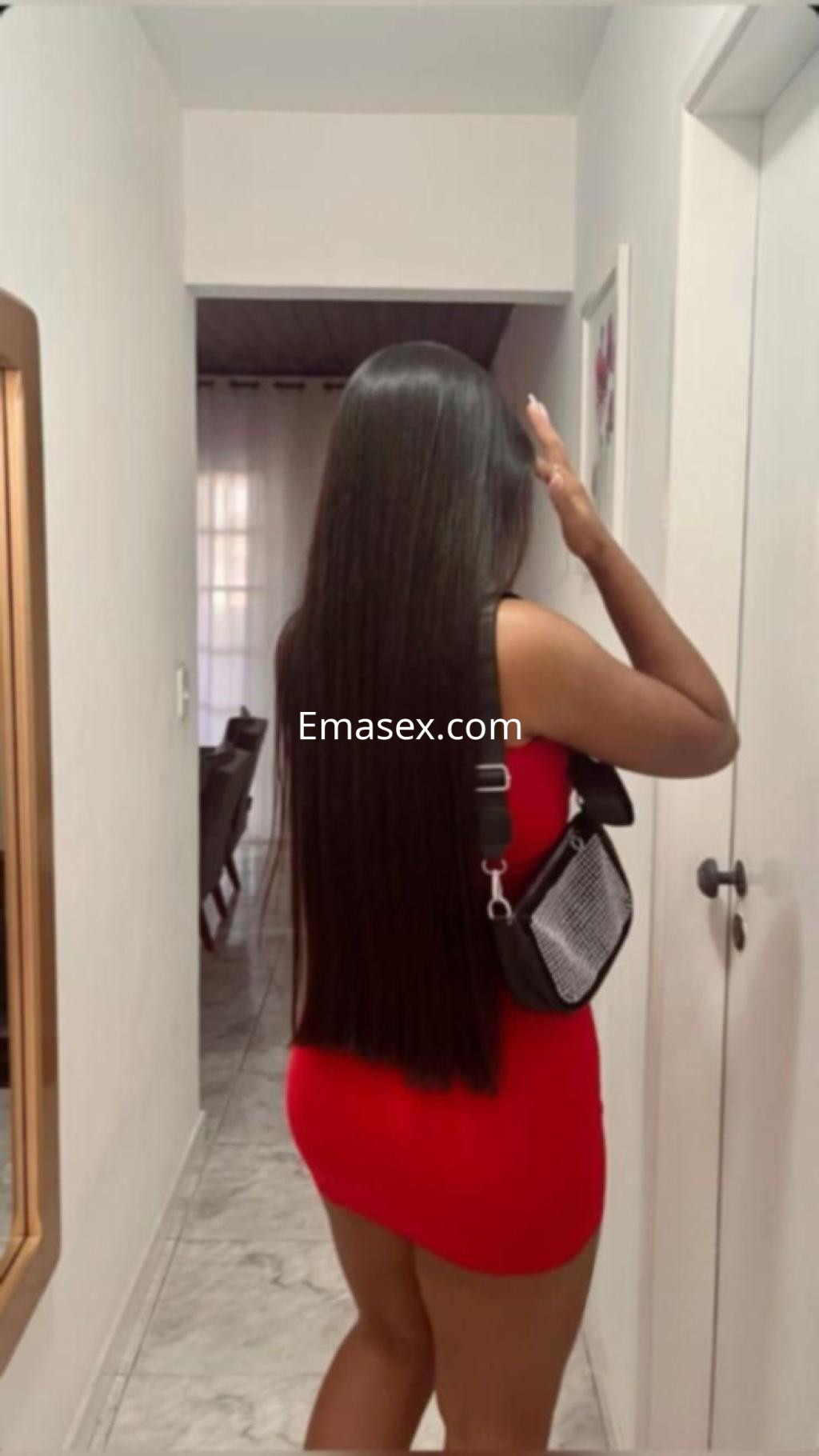 Puta con vestido rojo ajustado y cabello largo, de espaldas en un pasillo de un apartamento en Murcia.