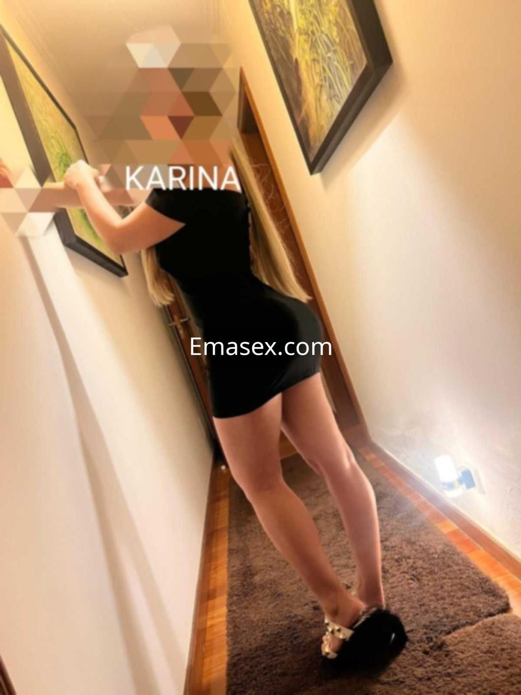 Puta en Pontevedra viste un ajustado vestido negro, posando de espaldas en un pasillo iluminado.