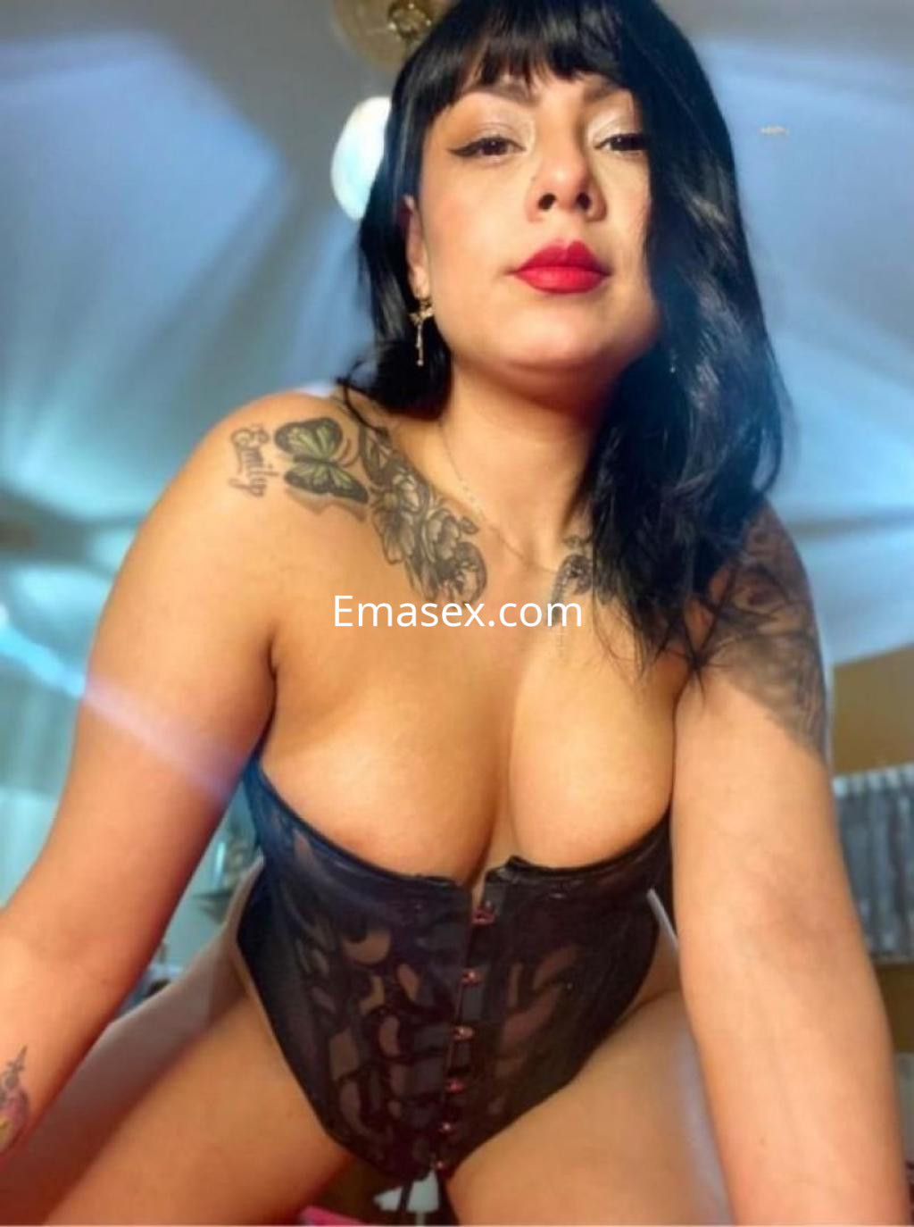 Puta en Tarragona, luciendo un corset negro ajustado, con cabello oscuro y labios rojos, en un ambiente iluminado.