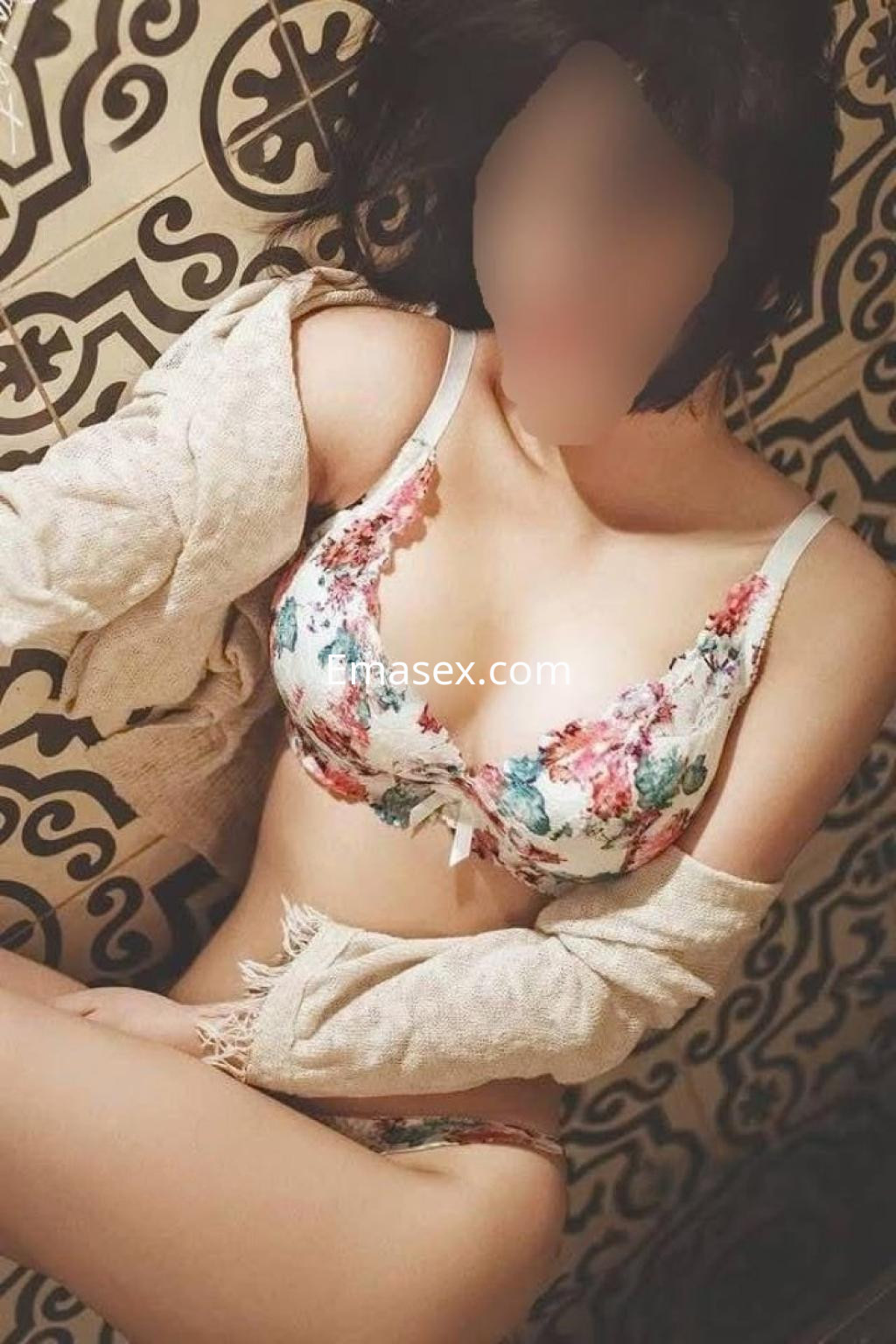Puta en Tarragona posando con lencería floral y una chaqueta ligera sobre un fondo decorativo.