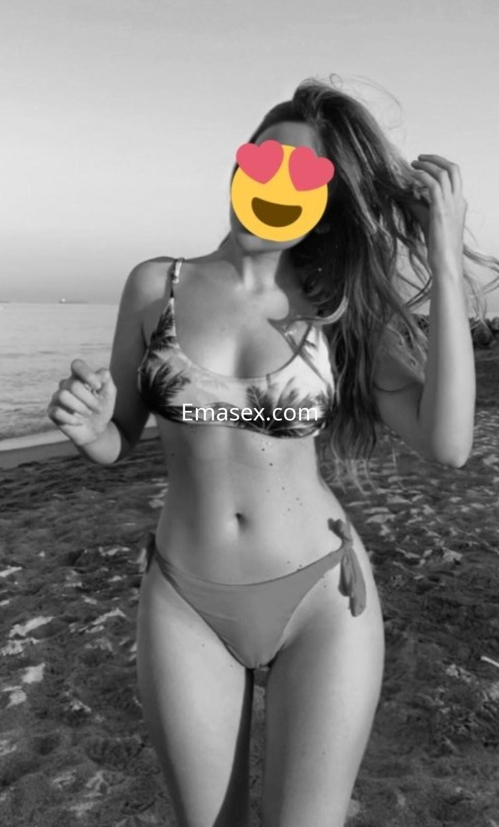 Escort en Vigo con cabello largo y suelto, luciendo un bikini de estampado tropical en la playa al atardecer.