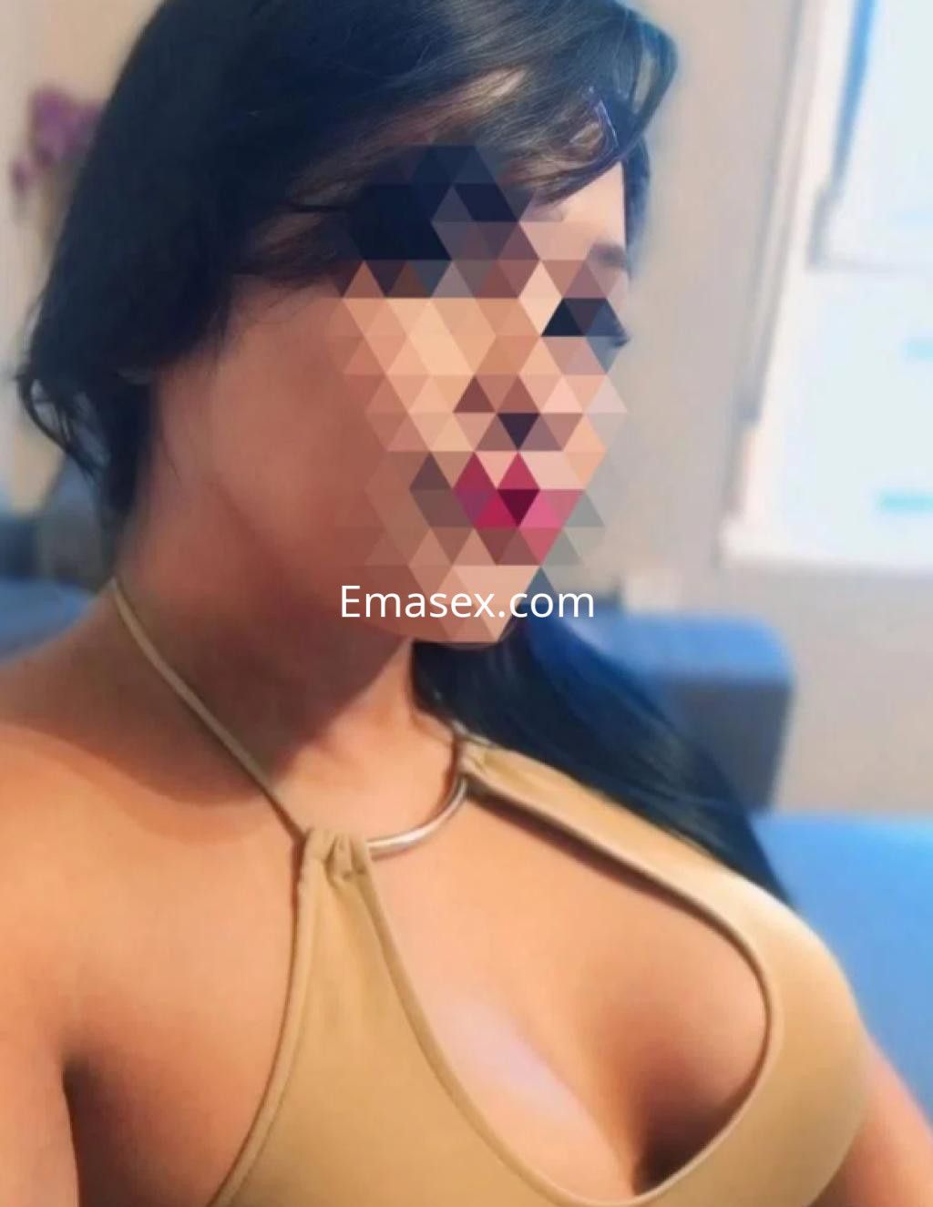 Puta en Gijón con top marrón que realza su figura, posando con una sonrisa en un entorno interior acogedor.