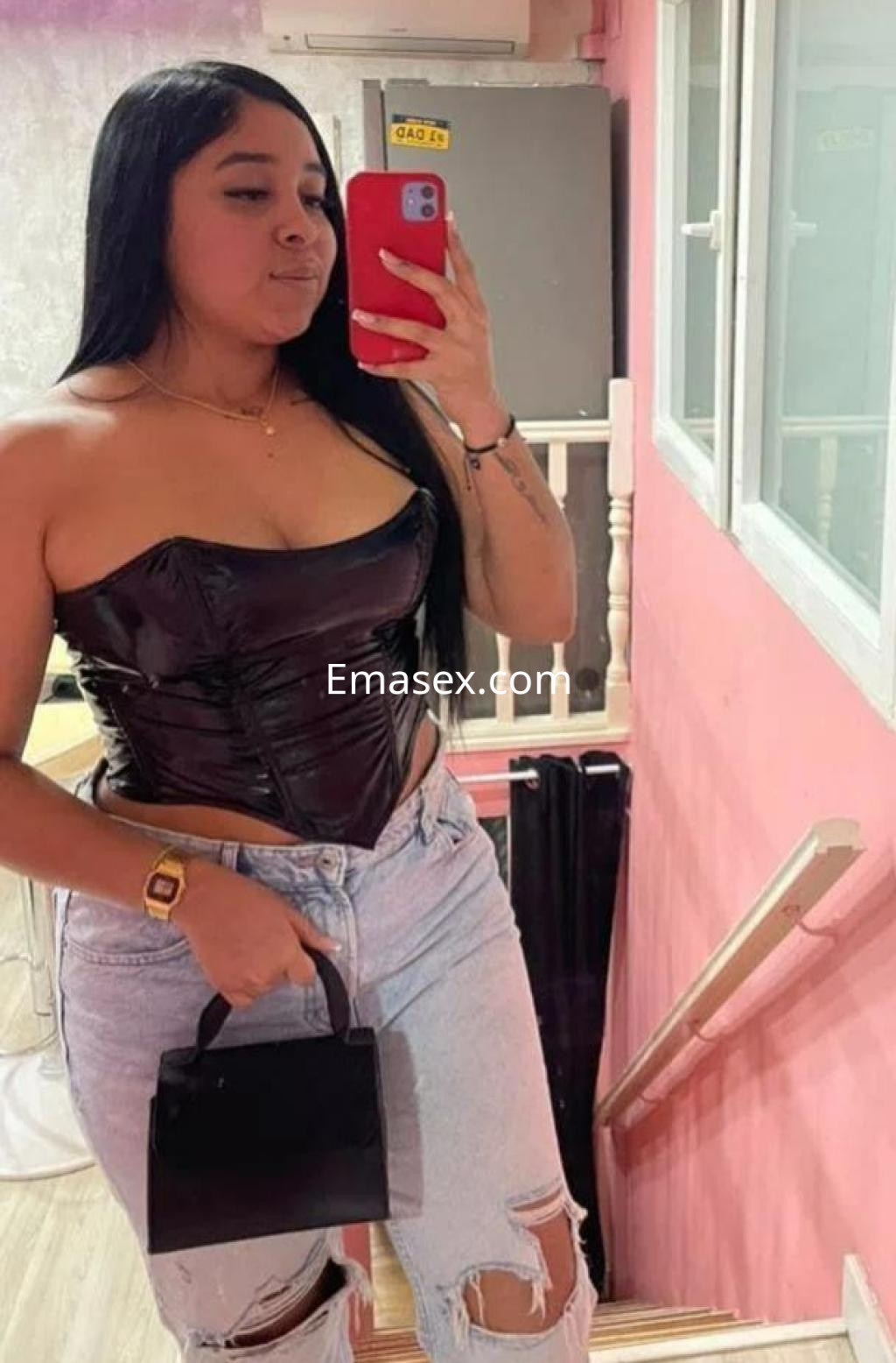 Escort en Castellón posando con un corset negro y jeans rasgados, sosteniendo un bolso pequeño.