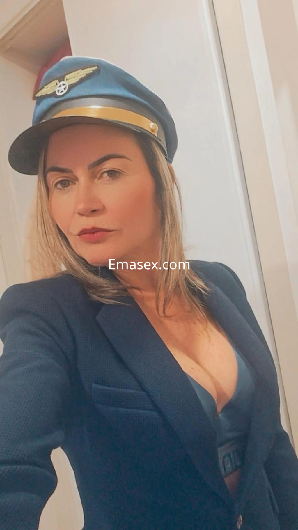 Escort en Santiago con cabello largo y rubio, vistiendo un traje de piloto y gorra, posando con actitud.