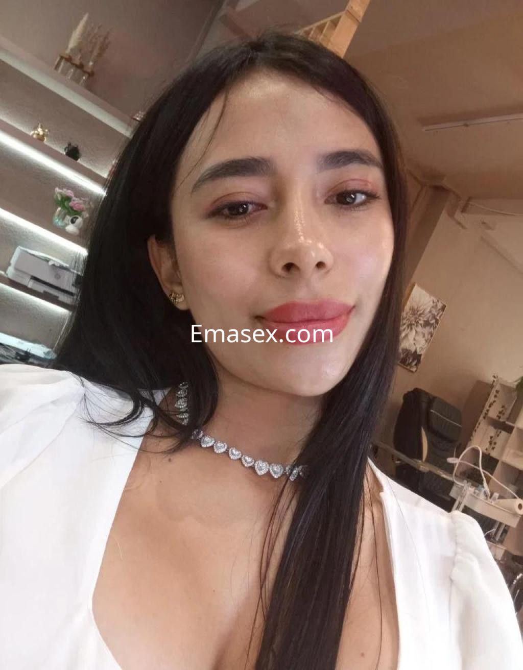 Escort en Badajoz con cabello largo y lacio, luciendo un collar brillante y una blusa blanca en un entorno elegante.