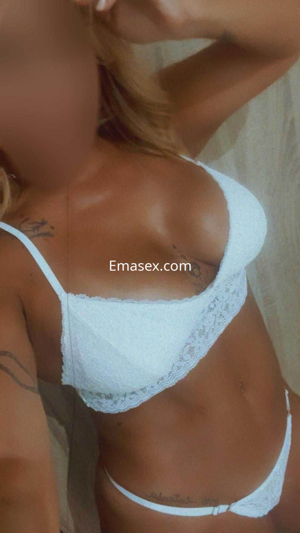 Puta en Badajoz posando con lencería blanca, mostrando su figura y tatuajes en un ambiente neutral.