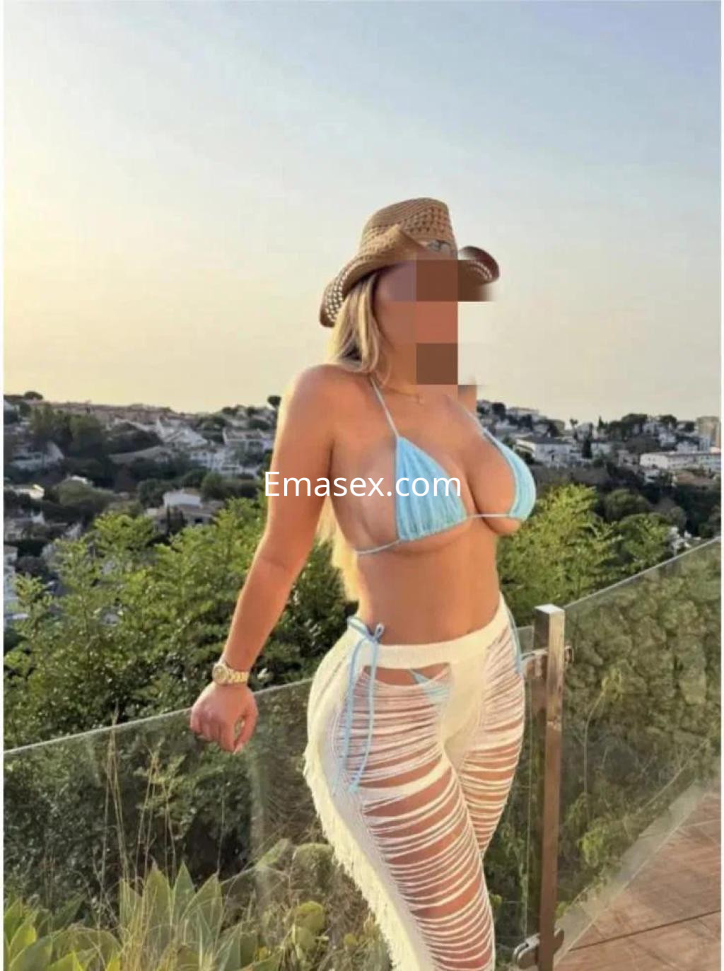 La escort en Cáceres luce un bikini azul y pantalones claros con cortes, disfrutando de un paisaje al atardecer.