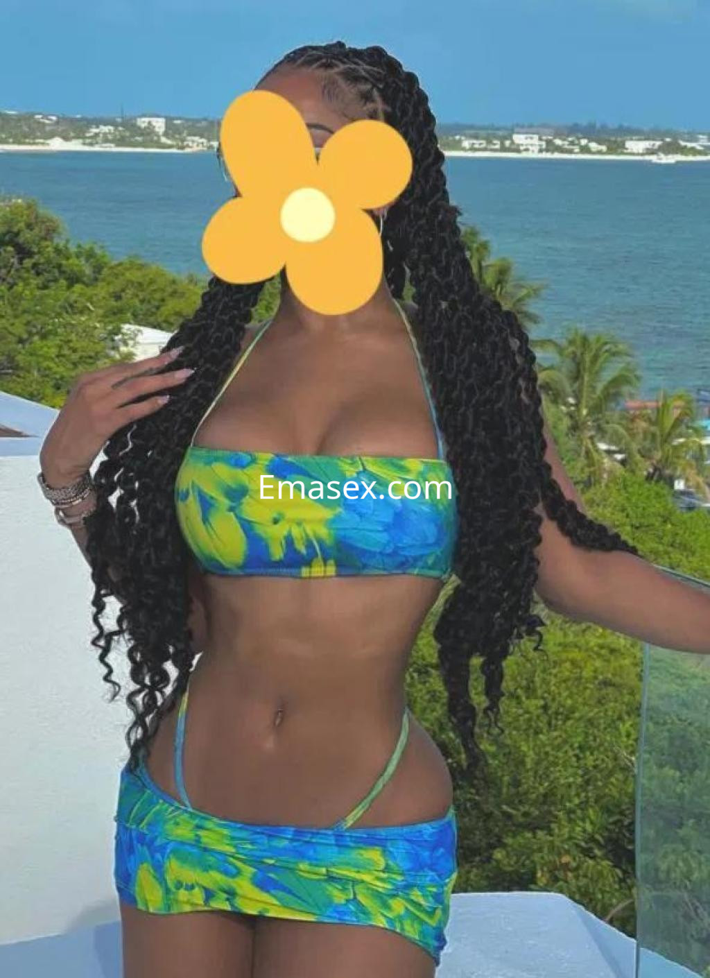 La puta luce un bikini colorido de tonos azules y verdes mientras posa frente a un paisaje costero en Alicante.
