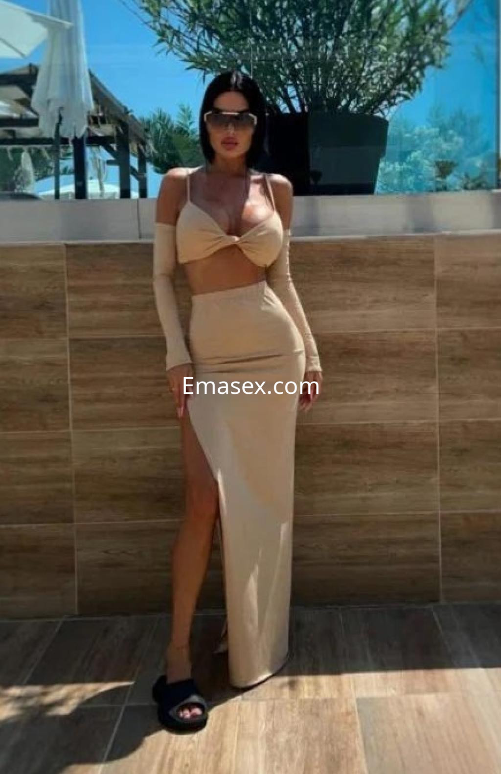 Puta en Alicante con un top beige que deja al descubierto el abdomen y una falda larga con una abertura lateral.