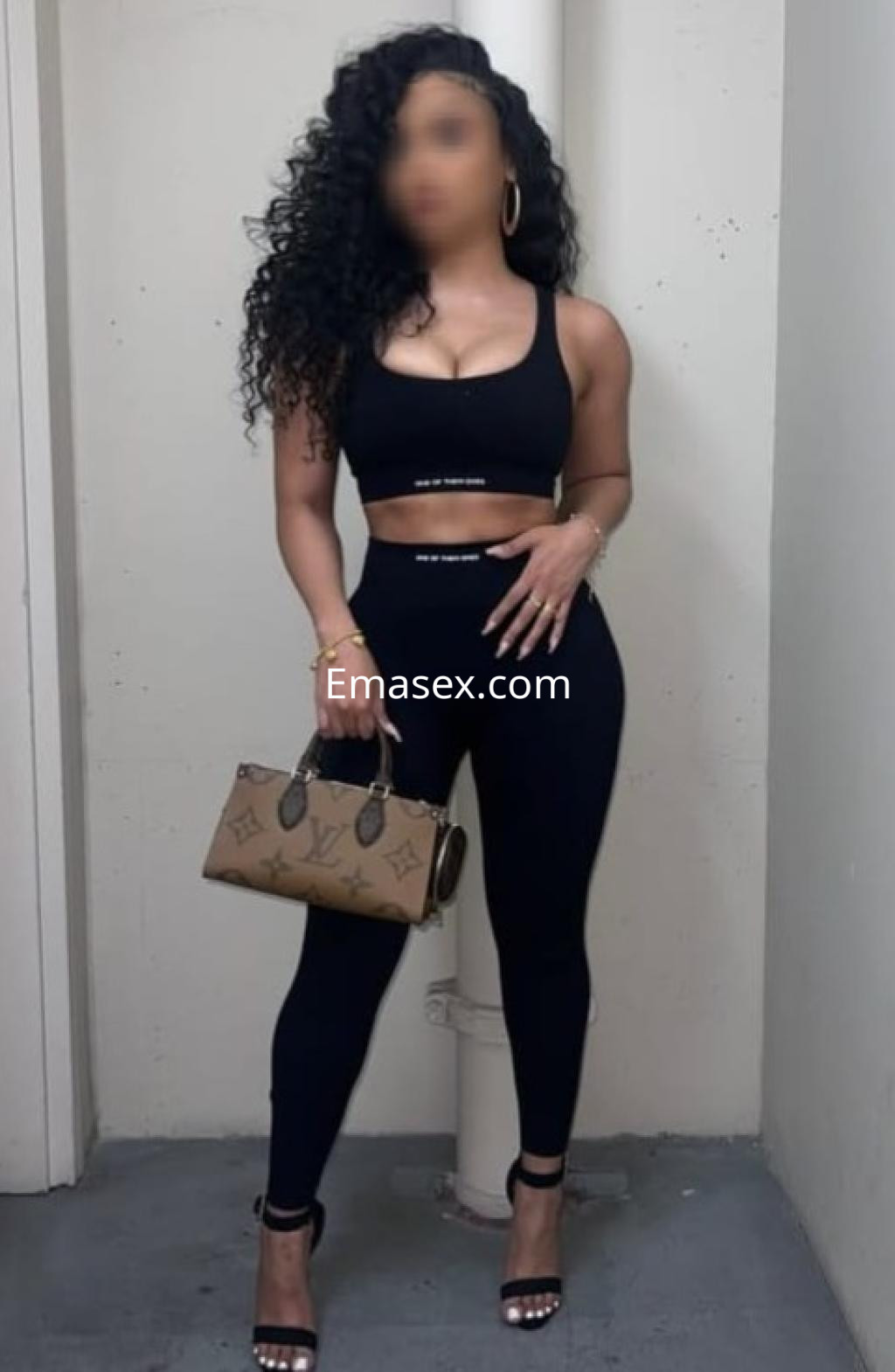 Escort en Donosti luciendo un top negro y leggings ajustados, con cabello rizado y un bolso elegante.