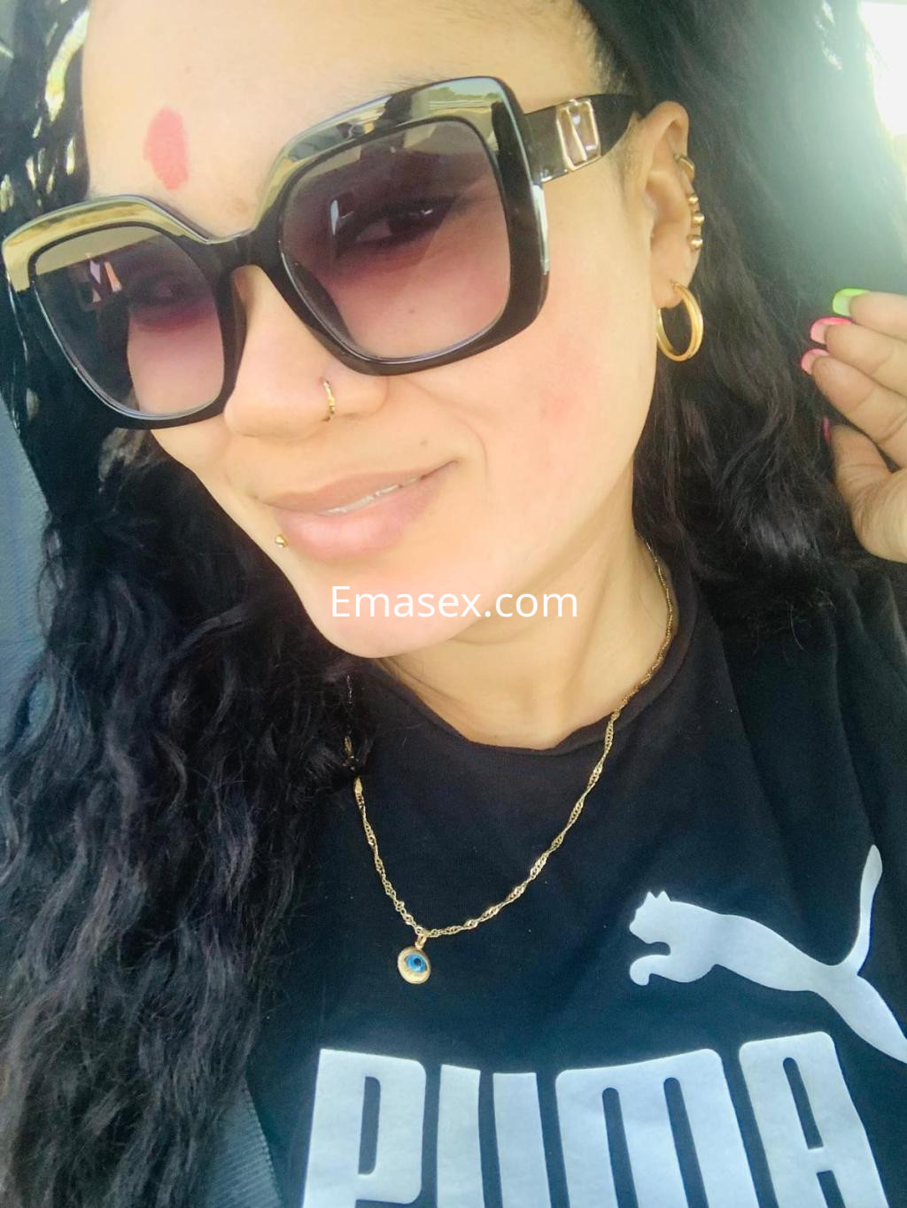 Puta con cabello rizado y oscuro, usa gafas de sol grandes y camiseta negra en un ambiente interior en León.